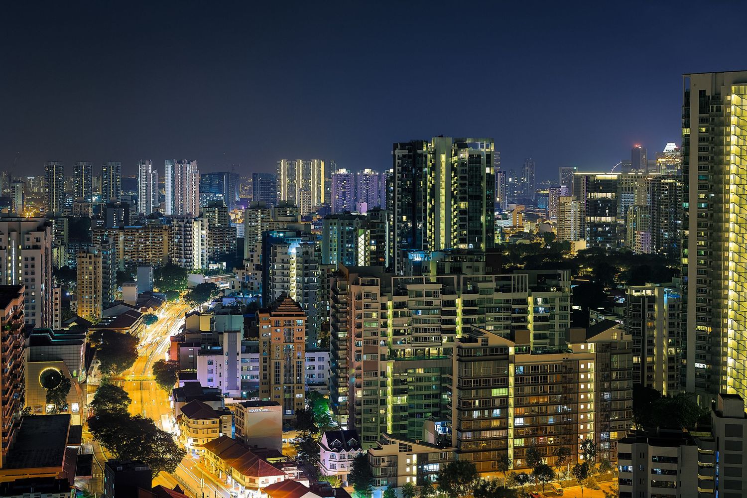 Aerial night view of a dense urban cityscape with illuminated skyscrapers and glowing streets in a modern Asian city.