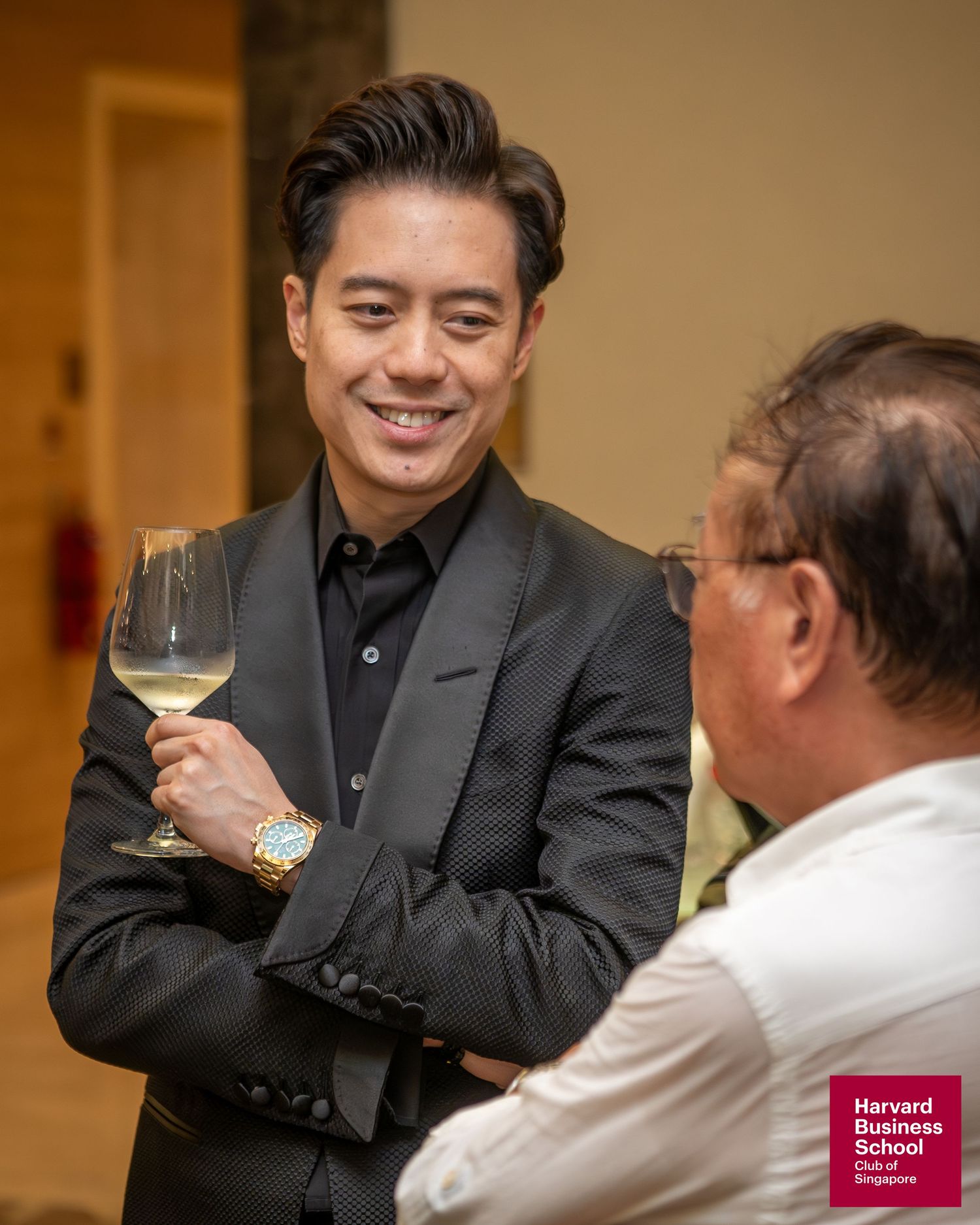 Man in black suit holding wine glass smiling at Harvard Business School Club event.