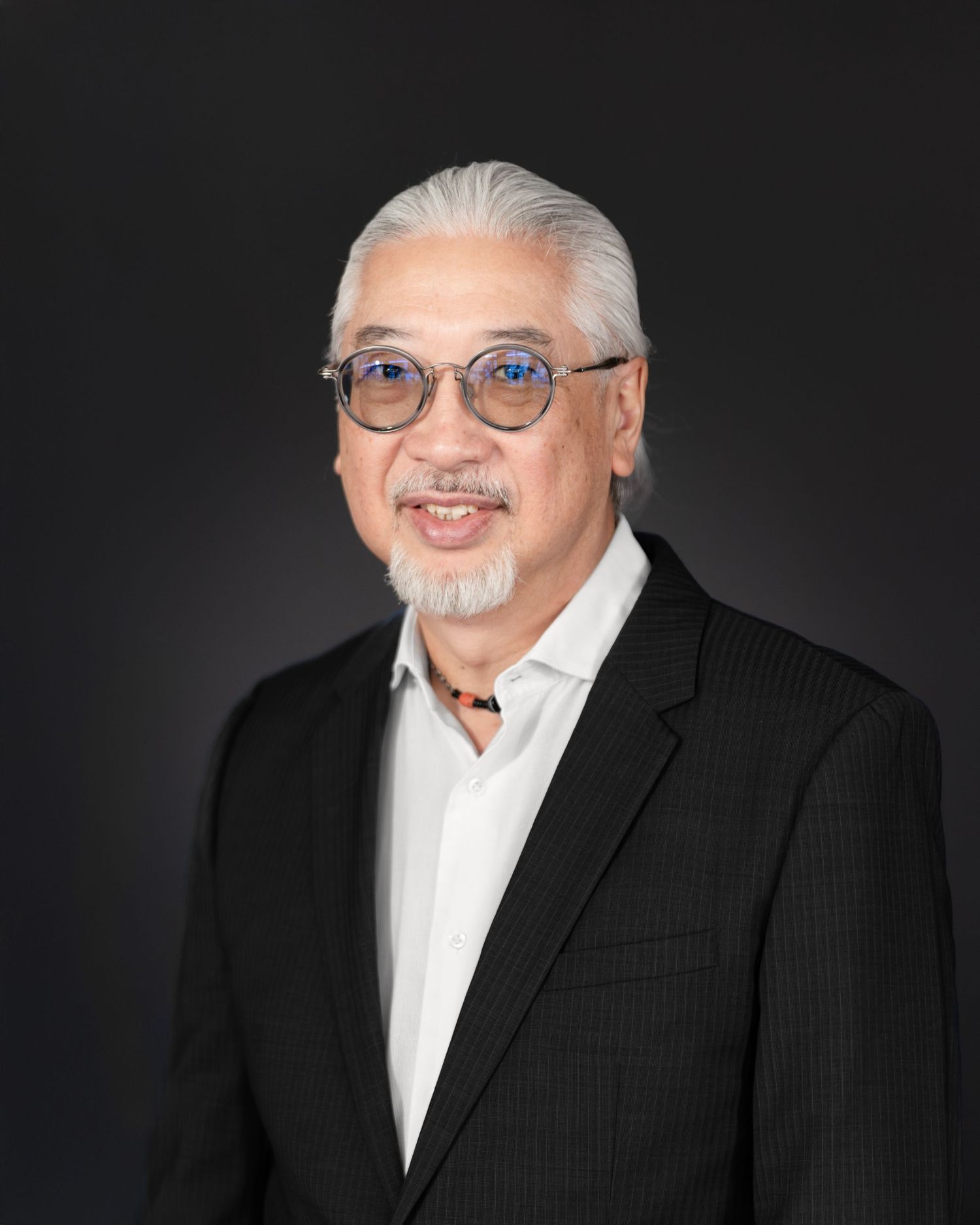 Distinguished older Asian man with gray hair in black blazer poses for professional headshot portrait.