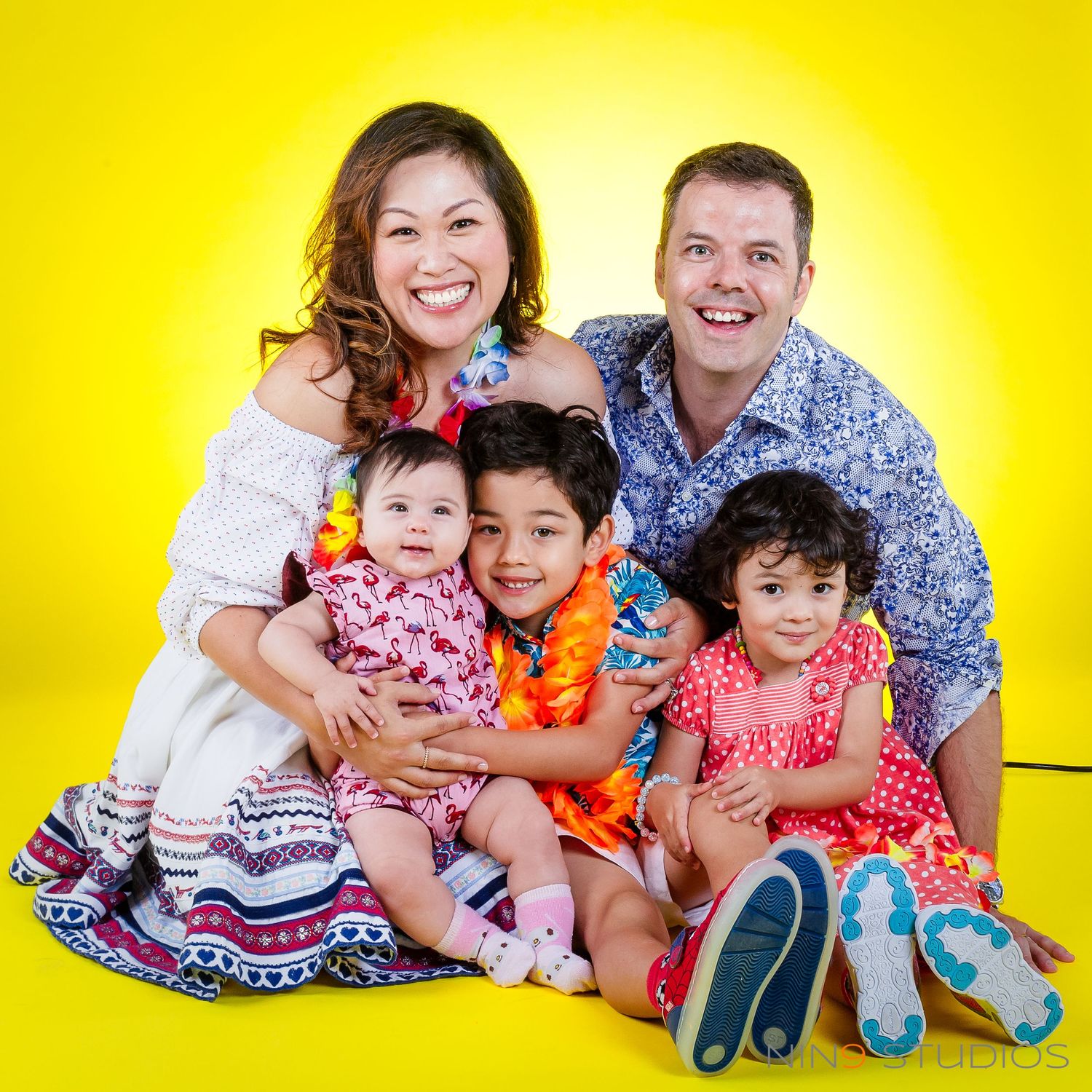 Happy family of five posing together against a bright yellow background in colorful outfits.