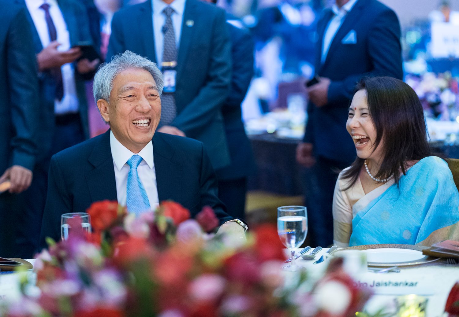 Two people sharing a laugh at a formal dinner event with floral centerpiece.