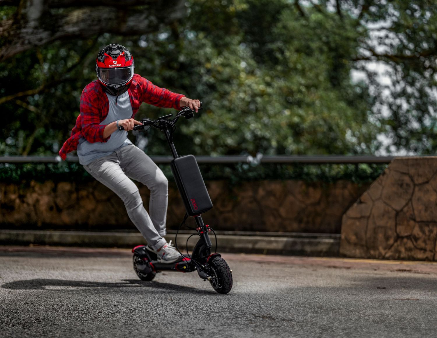 Person riding a black electric scooter wearing a red jacket and helmet on a road.