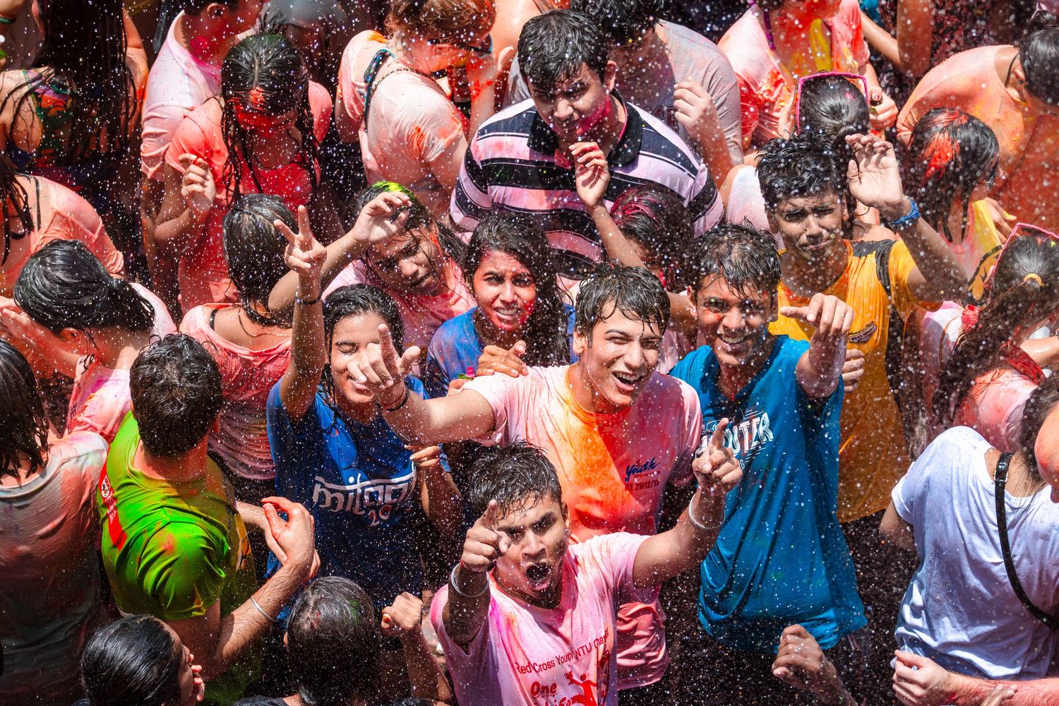 Crowd of young people celebrating and playing in colorful water and paint outdoors.