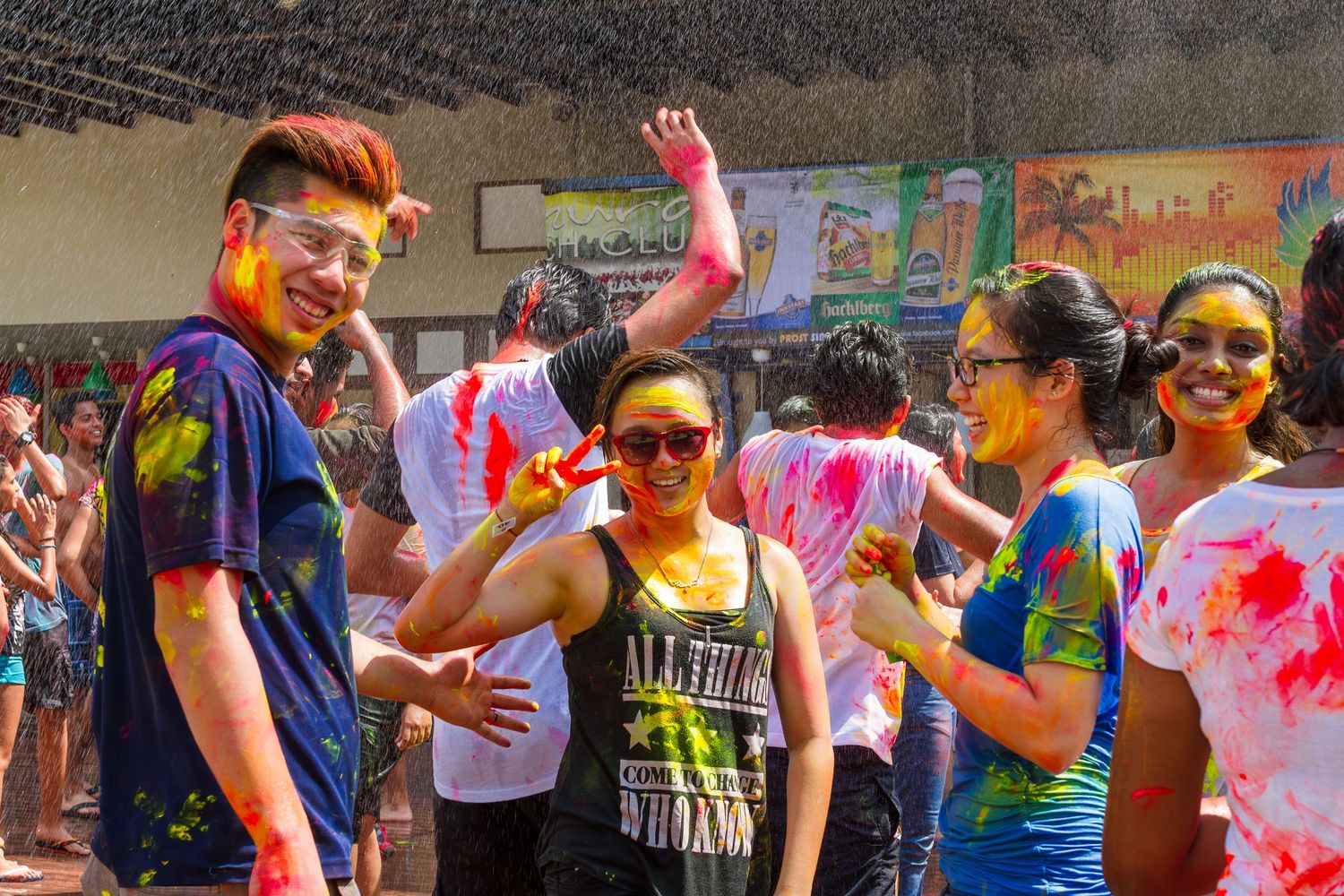 Group of friends smiling and covered in colorful powder during a lively Holi festival event.