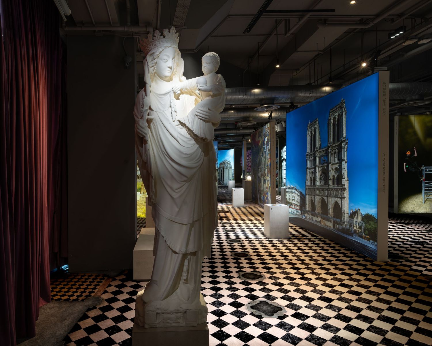 Museum exhibit with classical white statue, Notre Dame photography backdrop, and bold checkered black-and-white floor.