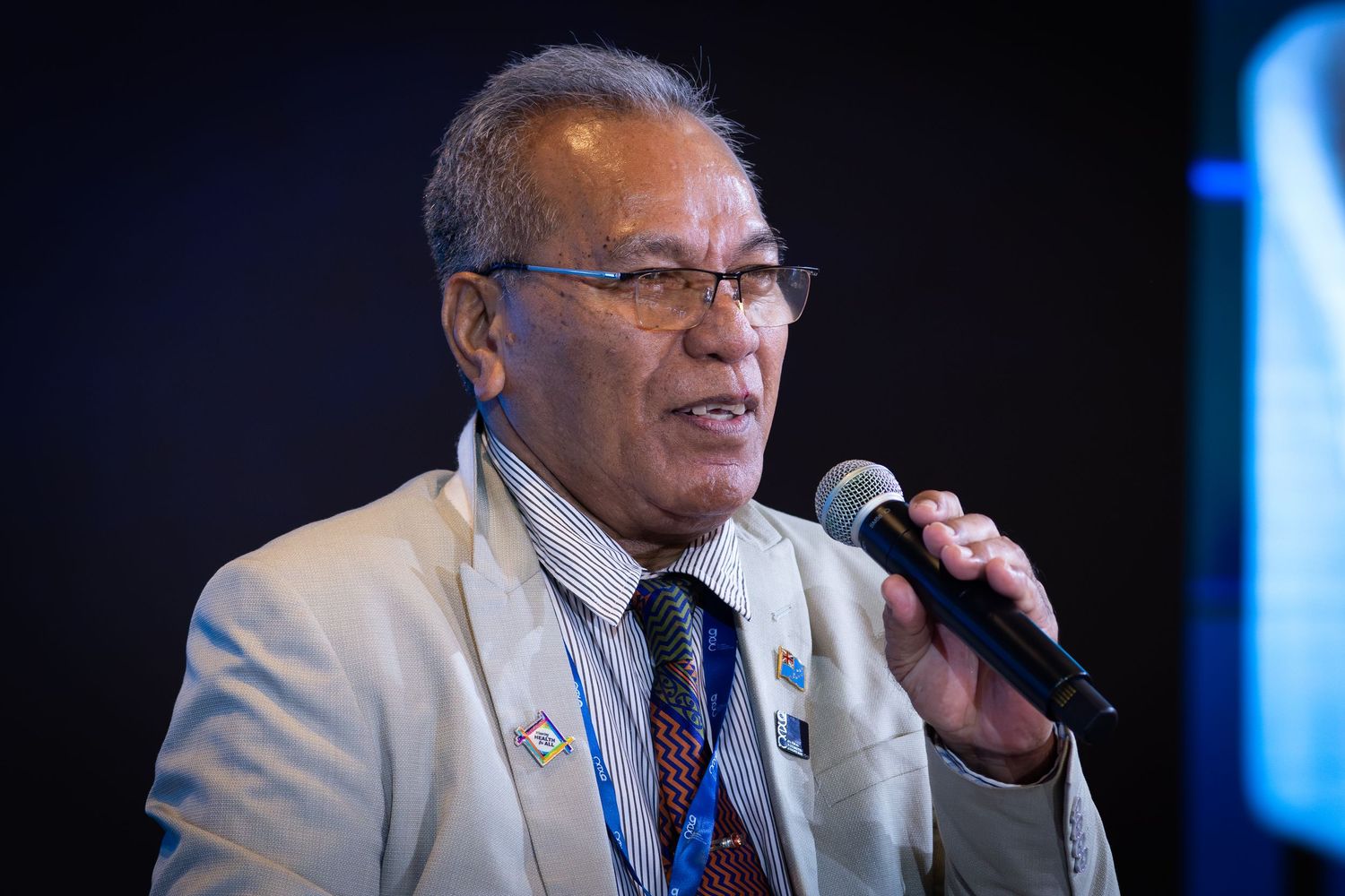 Senior man in suit speaks into microphone at a professional conference event.