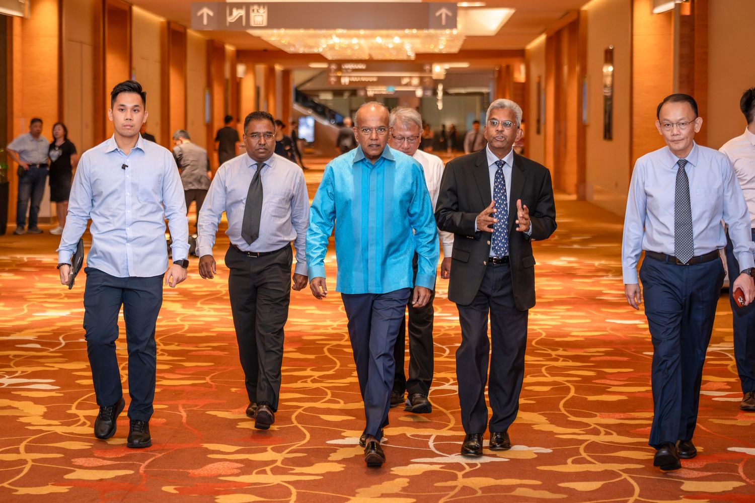 Group of five professionals walking confidently through elegant hotel corridor in Singapore.