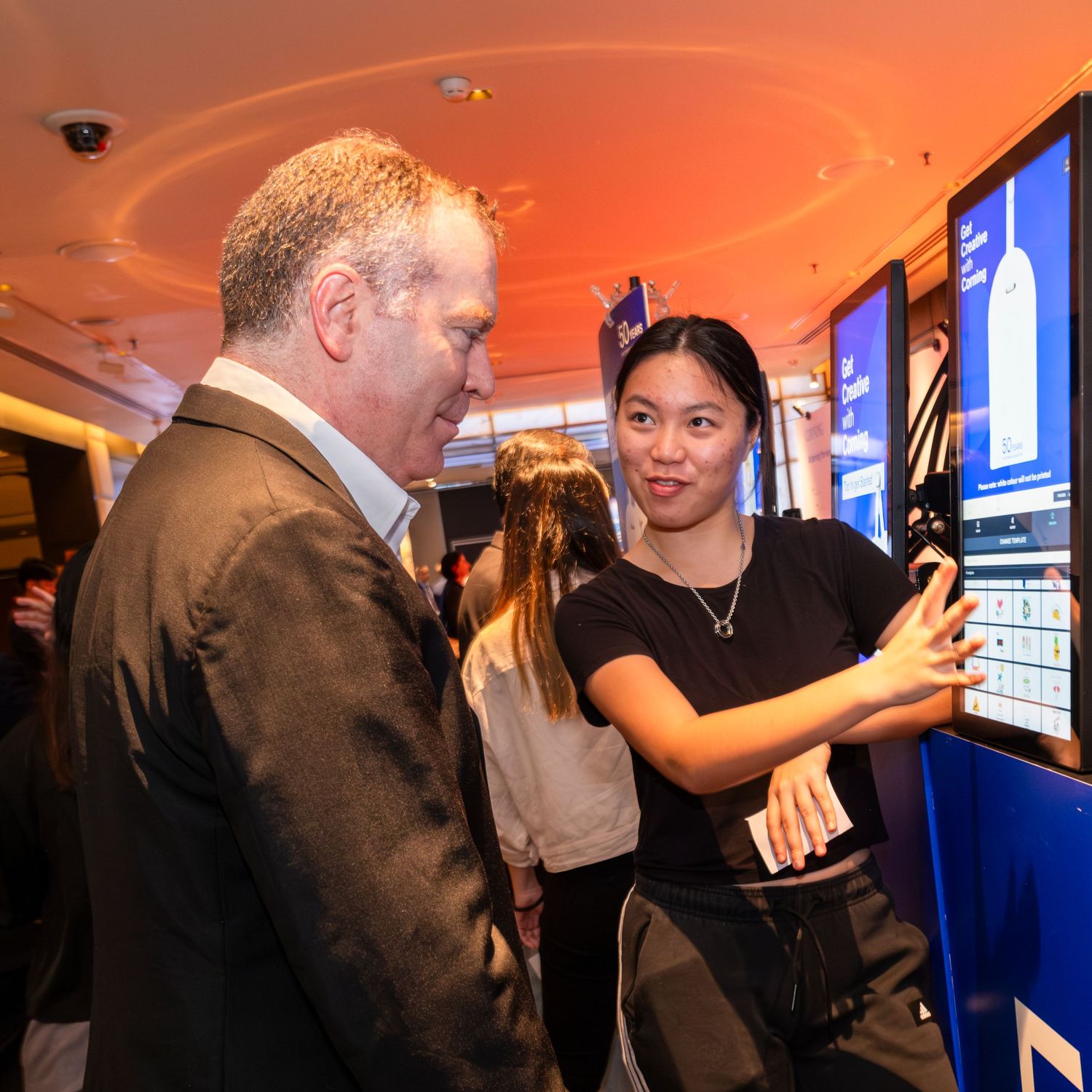 Young woman demonstrates interactive digital display screen to businessman at tech event.