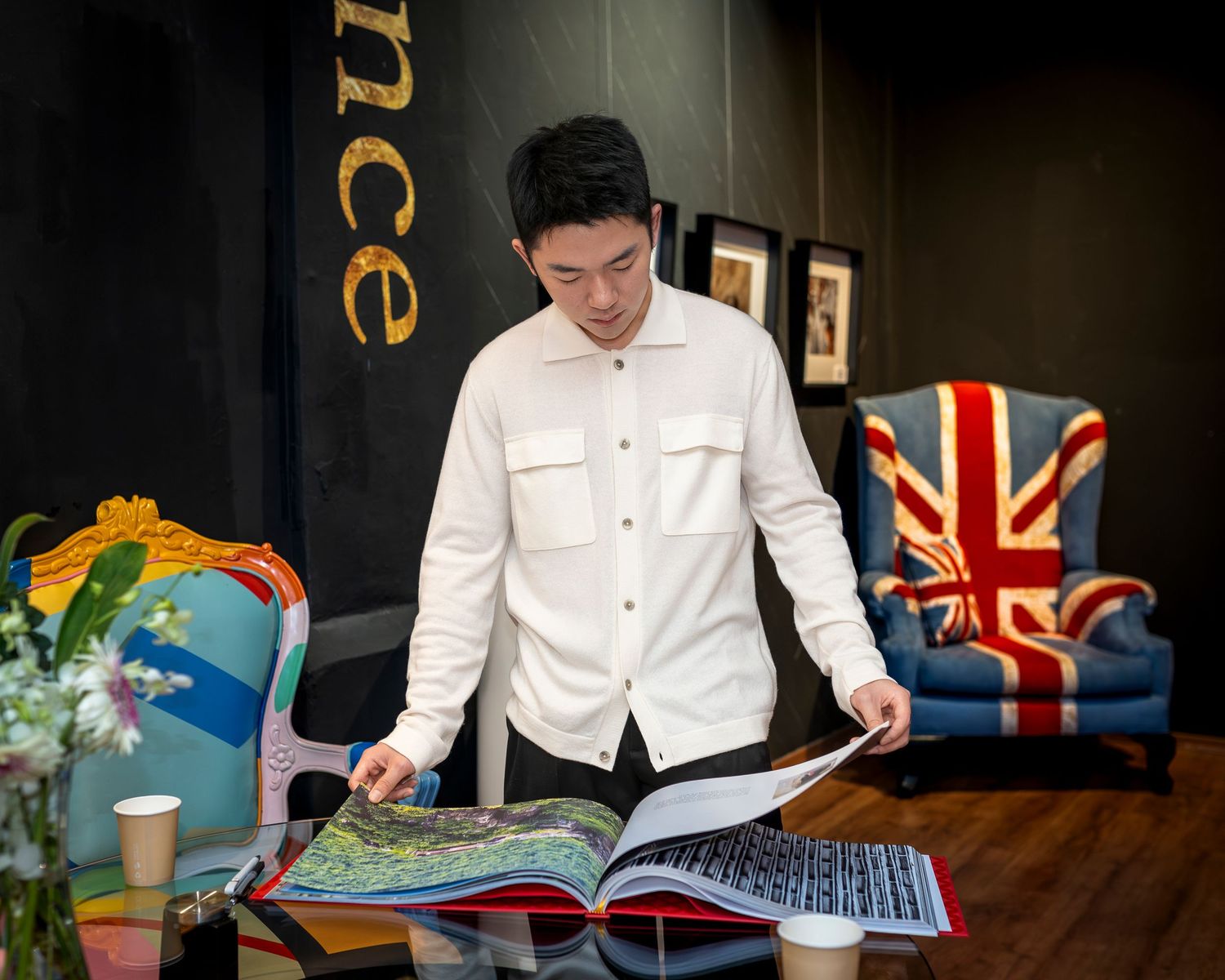 Young man in white shirt browses a large photography book in a decoratively styled room.