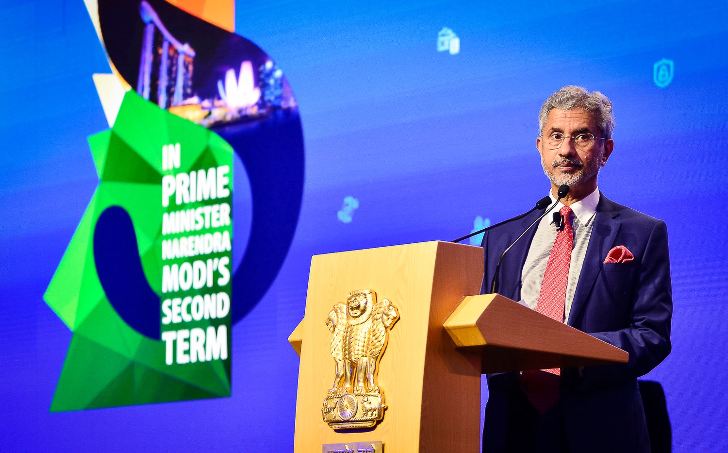 Indian official speaks at podium during Prime Minister Modi second term event with national emblem displayed.