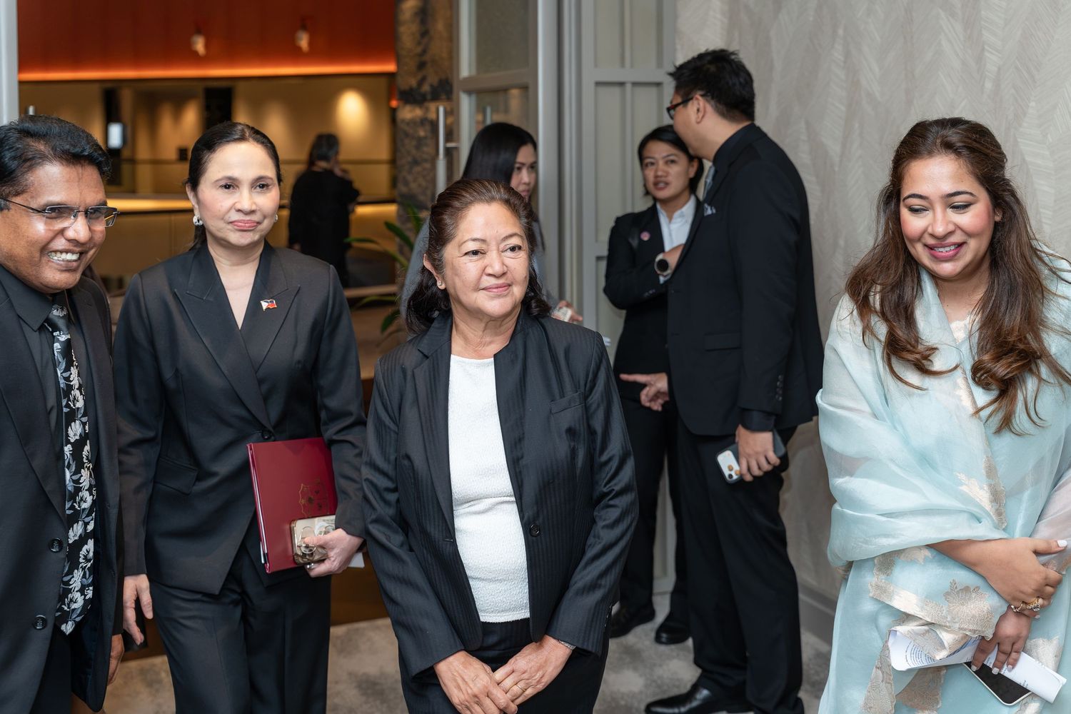 Group of professionals in formal attire walking through a modern building lobby at a corporate event.