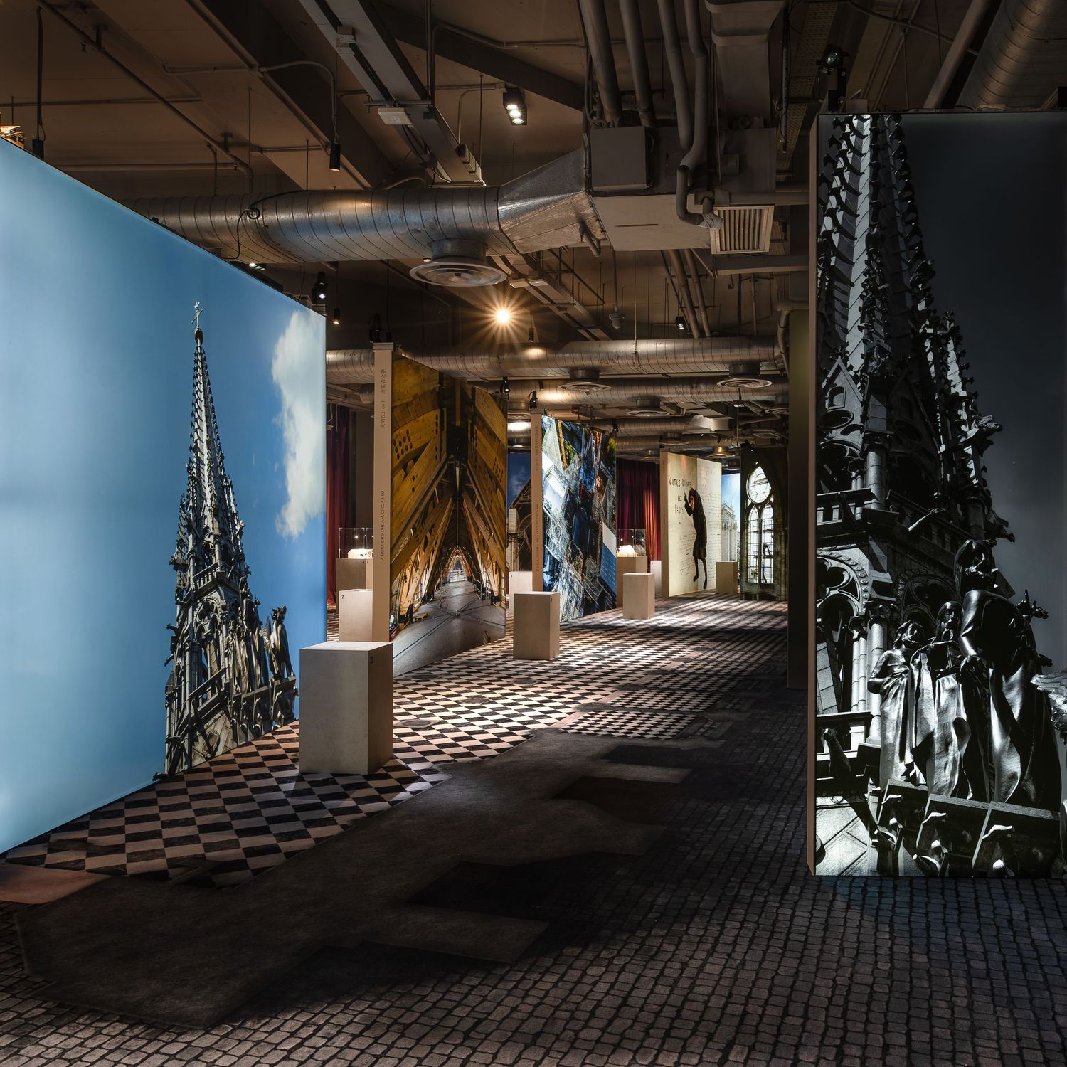 Gothic architecture museum exhibition with cathedral spire large-scale prints and checkered tile floor.