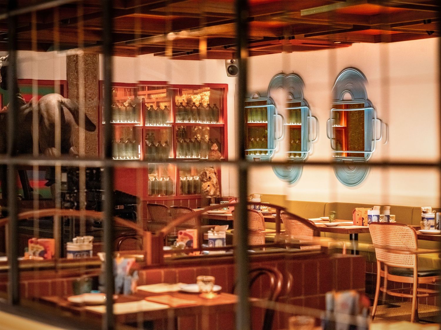 Warm-toned restaurant interior viewed through glass grid, featuring a well-stocked bar, booth seating, and decorative wall art.