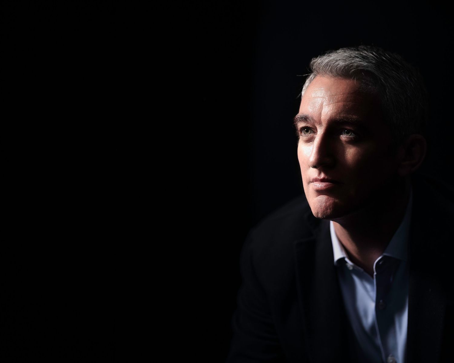 Dramatic low-light portrait of a man in dark jacket with moody shadows and contrast.