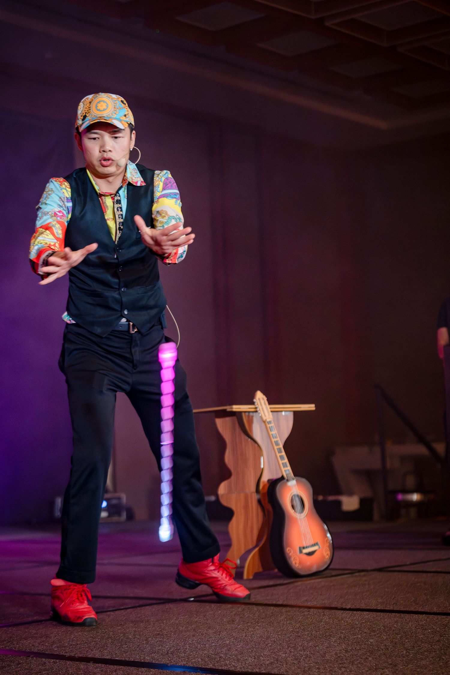 Performer in colorful outfit and cap dancing on stage with a ukulele prop and LED light stick behind them.