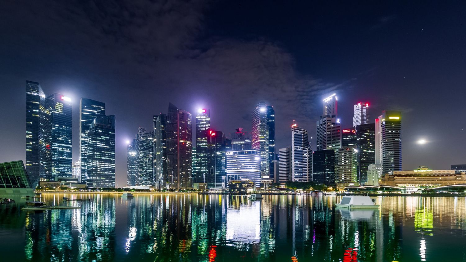 Singapore city skyline illuminated at night reflecting in Marina Bay waters with skyscrapers.