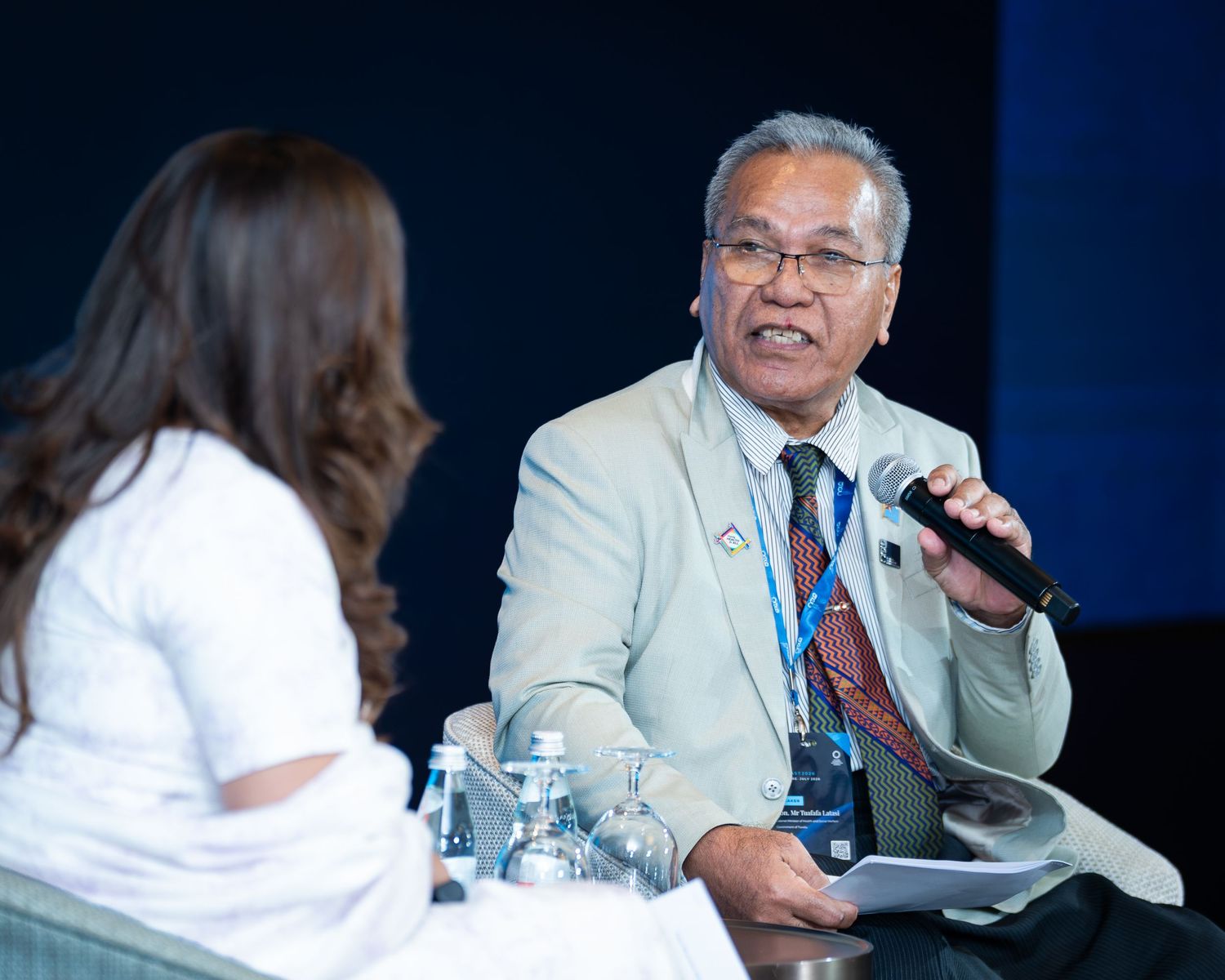 Senior male speaker holding microphone at a panel discussion during a professional conference.