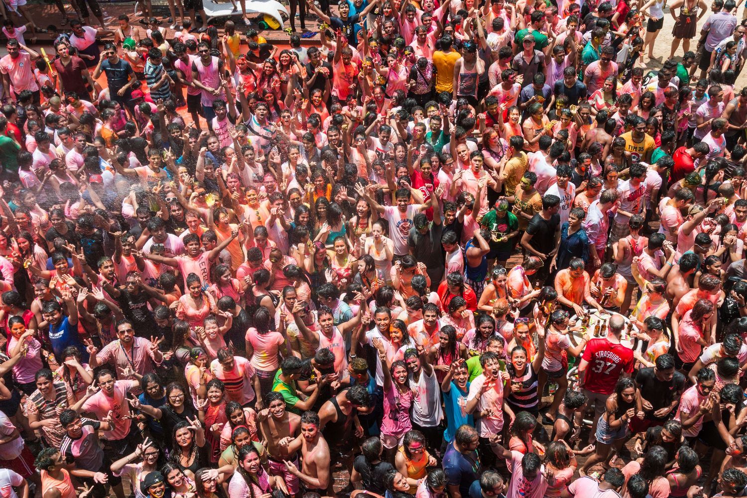 Aerial view of large crowd celebrating Holi festival covered in vibrant colored powder.
