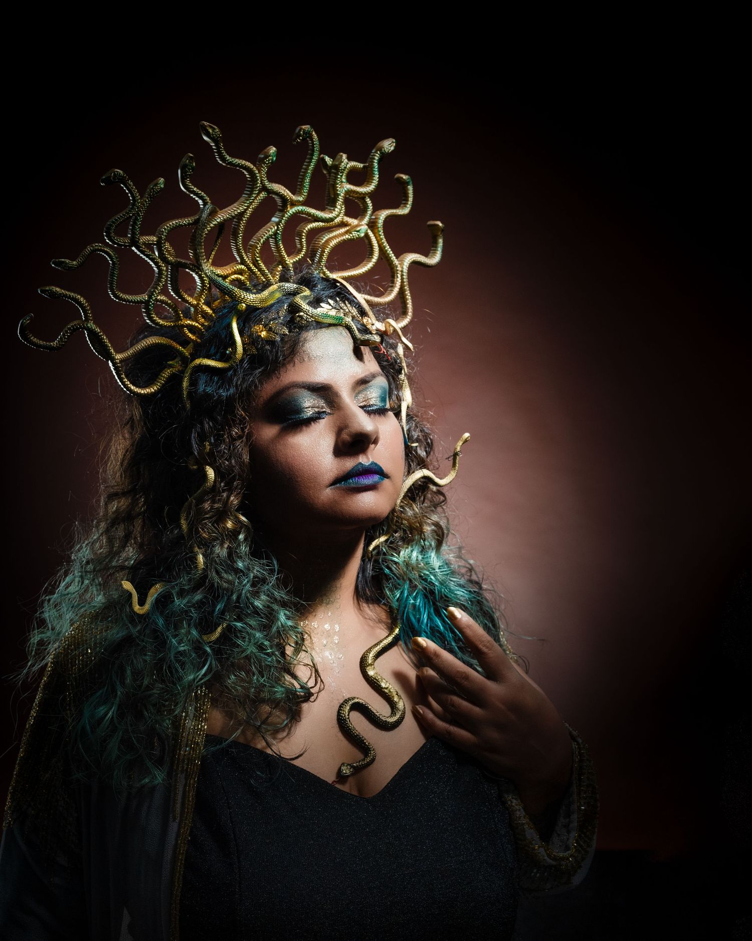 Woman dressed as Medusa with golden snake headpiece, teal curly hair, blue lips, and dramatic fantasy makeup.