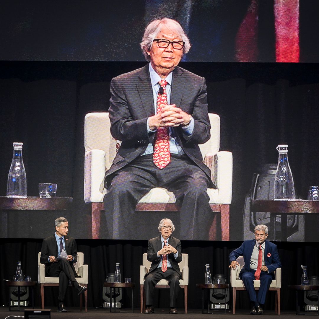 Panel discussion on stage at business conference with four executives seated in white chairs.