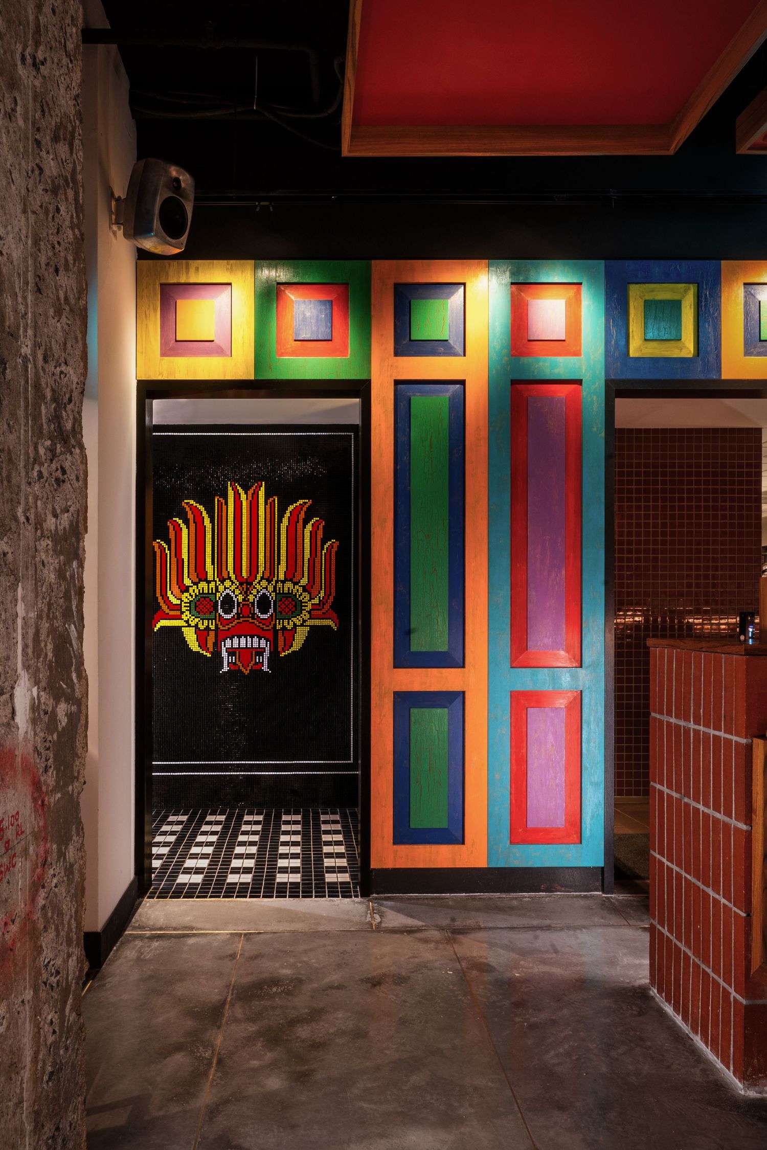 Vibrant colorful corridor with multicolored panels and traditional demon mask artwork on black door.