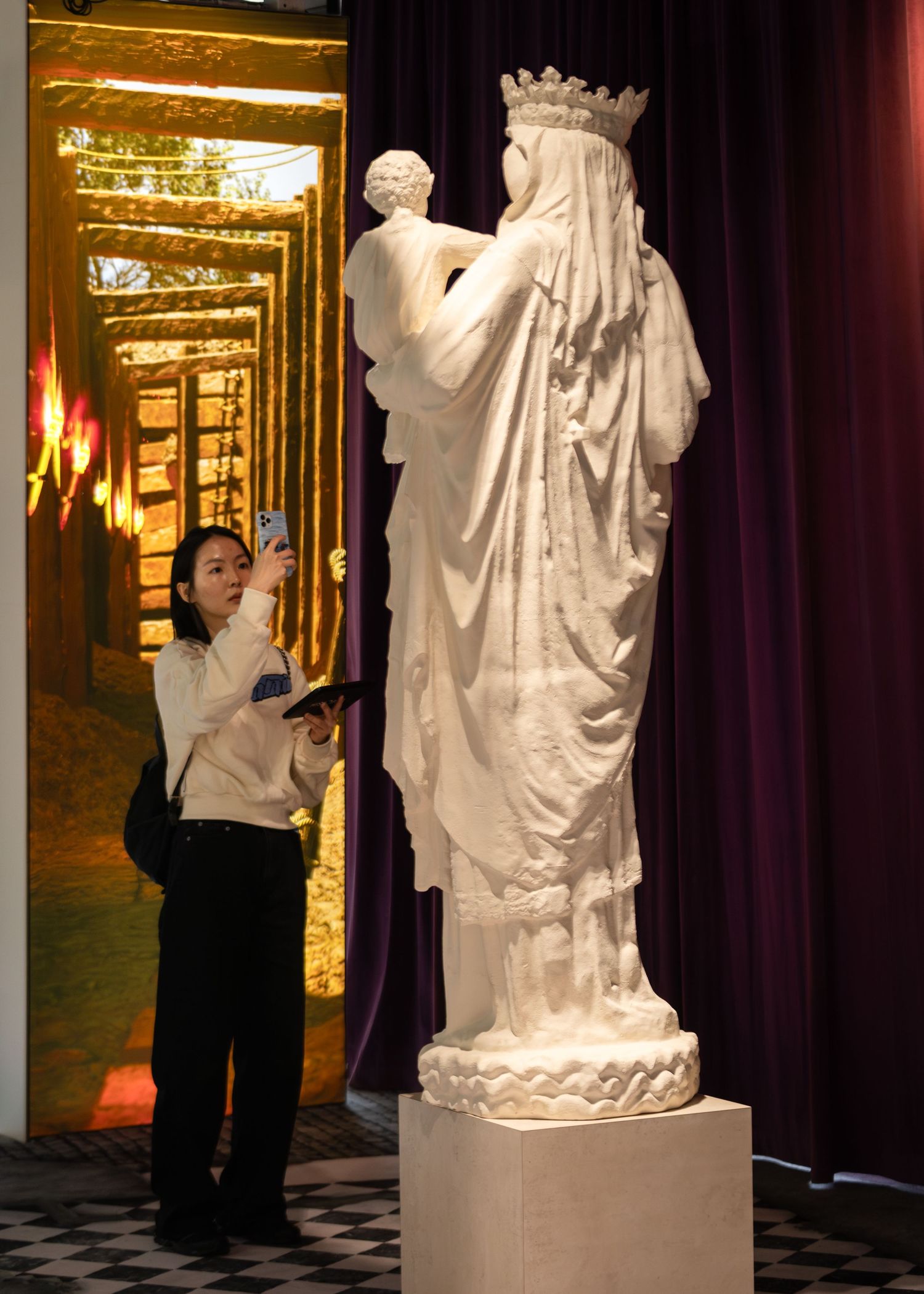 Woman photographs ornate white marble Madonna and child statue at museum exhibition.