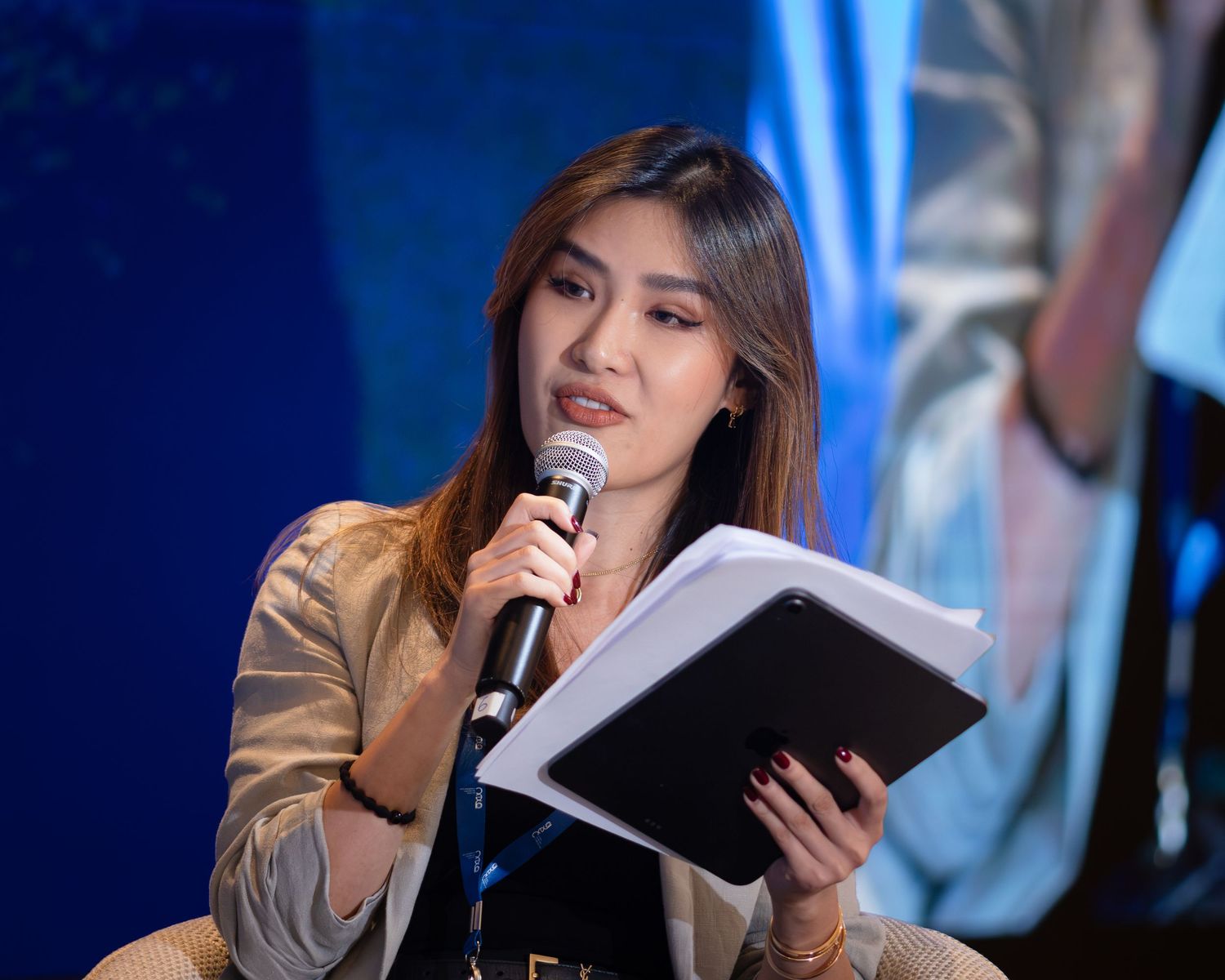 Young woman speaking into a microphone while holding papers at a professional conference or panel event.