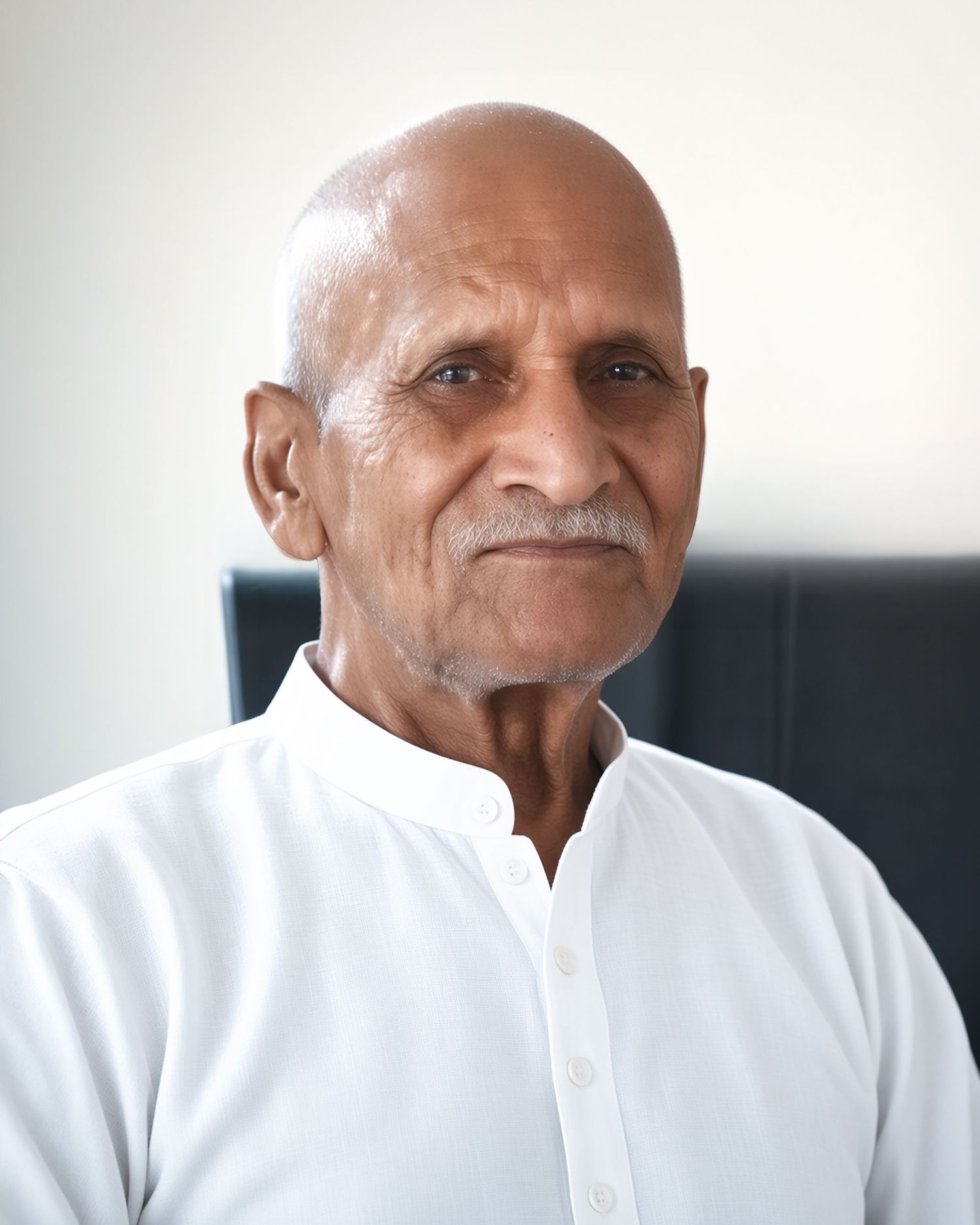 Elderly bald man with white mustache wearing a white shirt, portrait photo with light background.