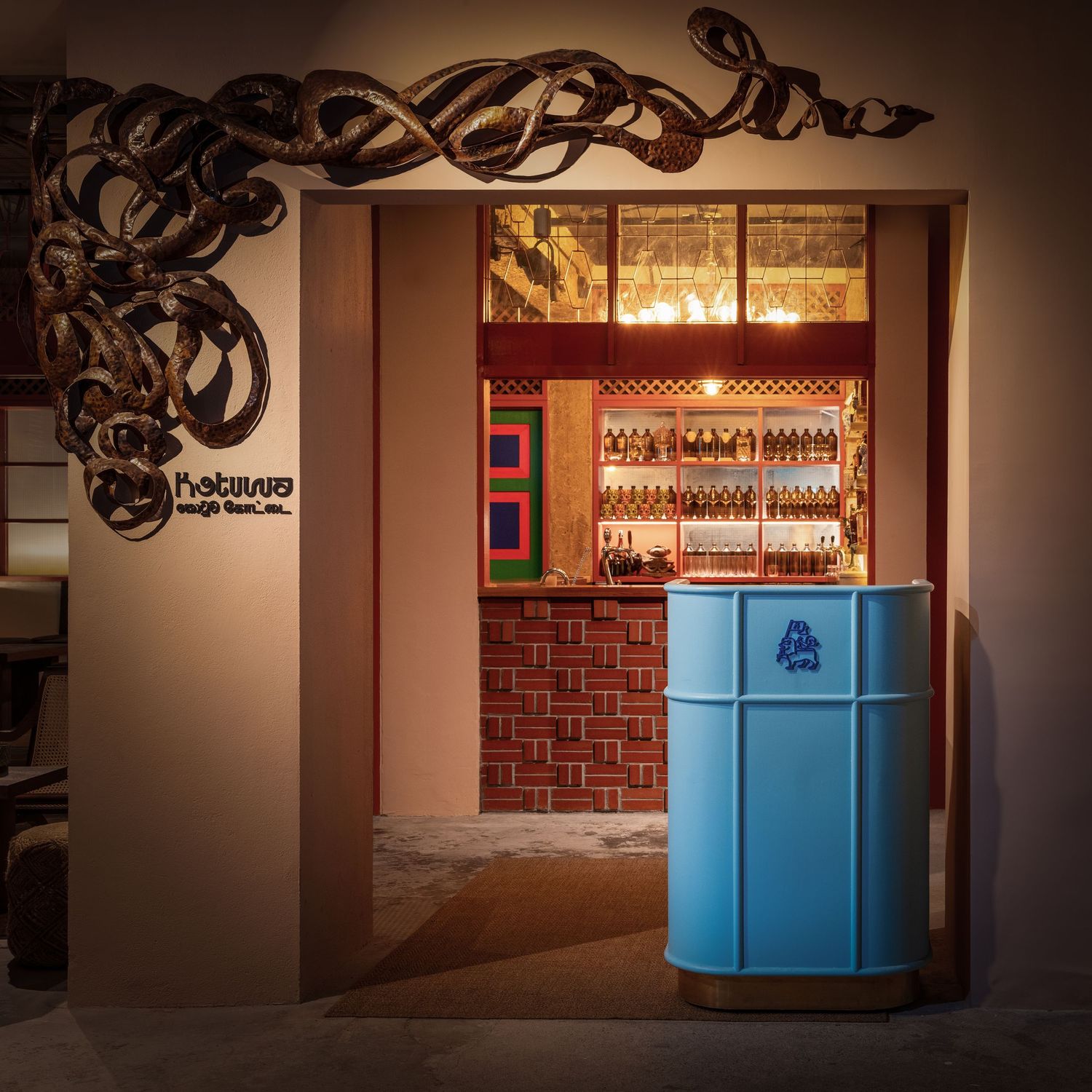 Blue barrel reception desk at a moody bar entrance with snake wall art and backlit liquor shelves.