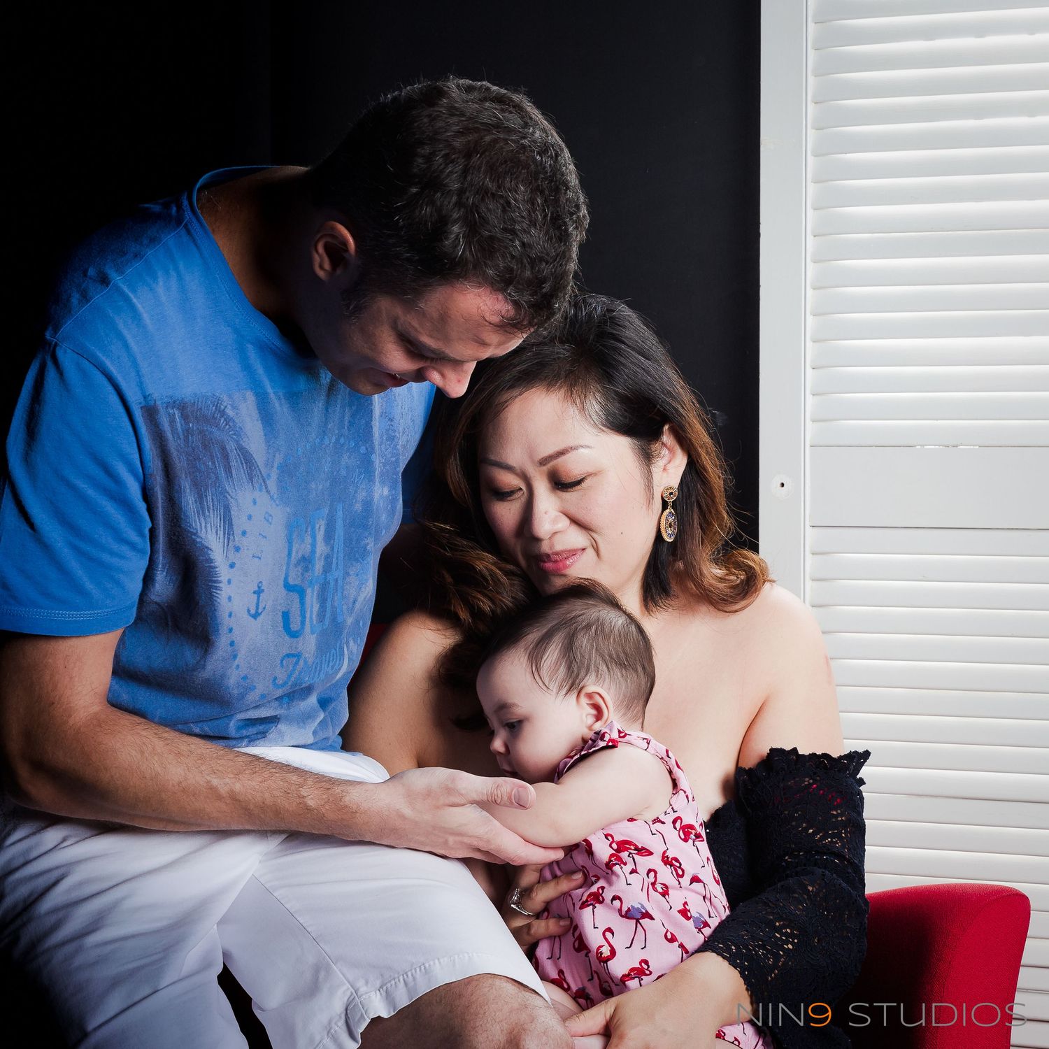 A family portrait of parents lovingly gazing at their baby girl in a cozy studio setting.