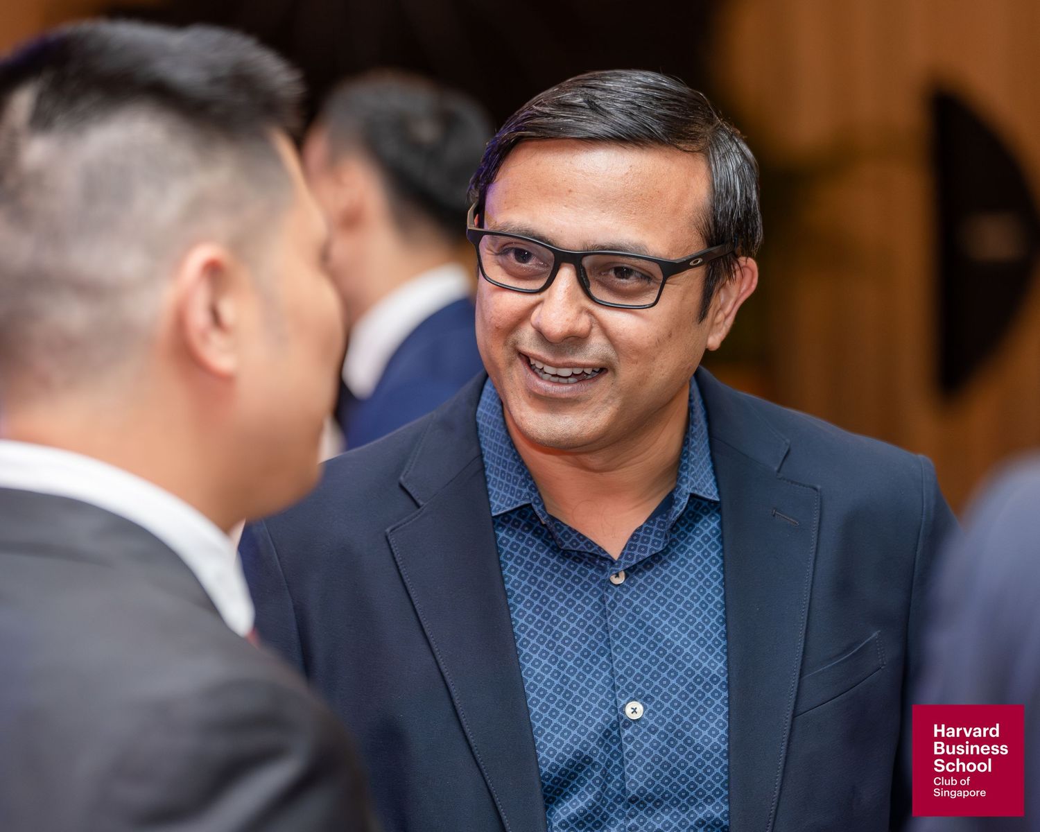 Professional man in blazer smiling during networking event at Harvard Business School Club of Singapore.