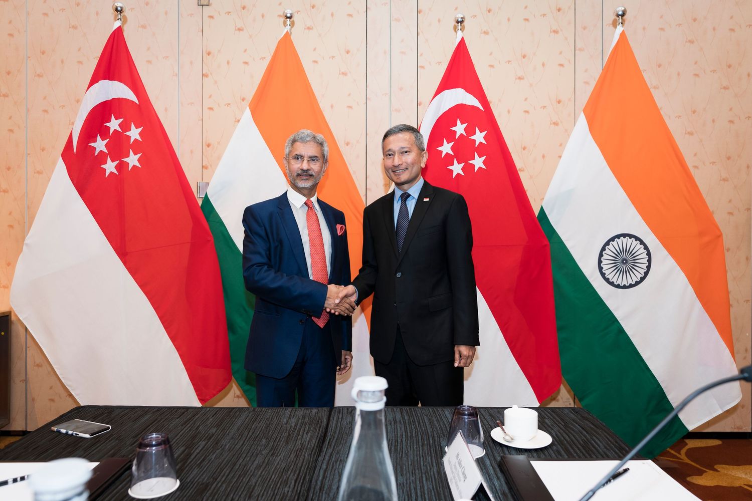 Two diplomats shake hands in front of Singapore and India national flags at a bilateral meeting.