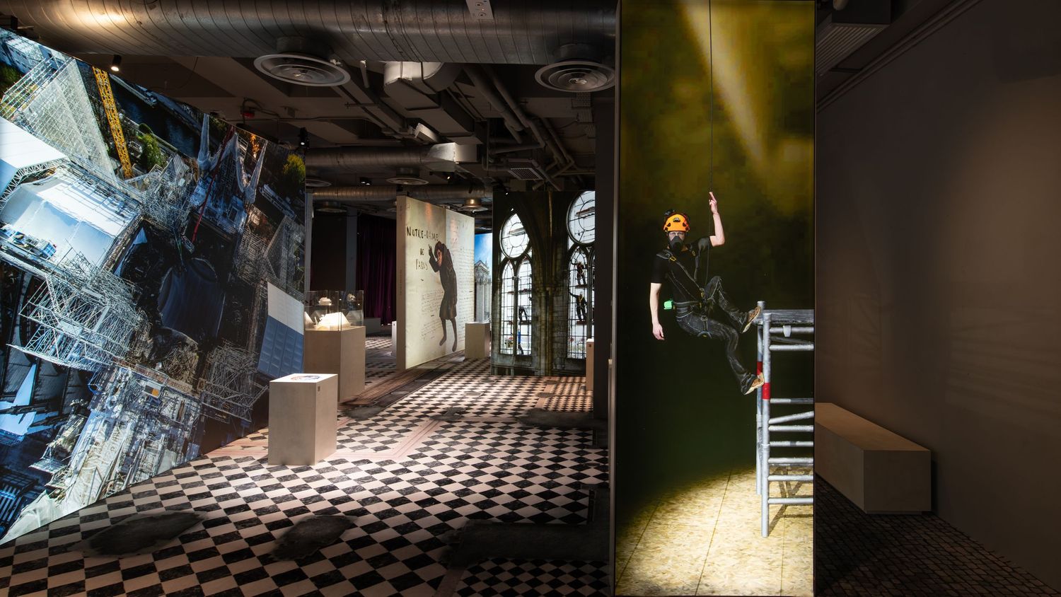 Modern art exhibition space featuring checkered floors, large digital installations, and dramatic lighting with a performer on stage.