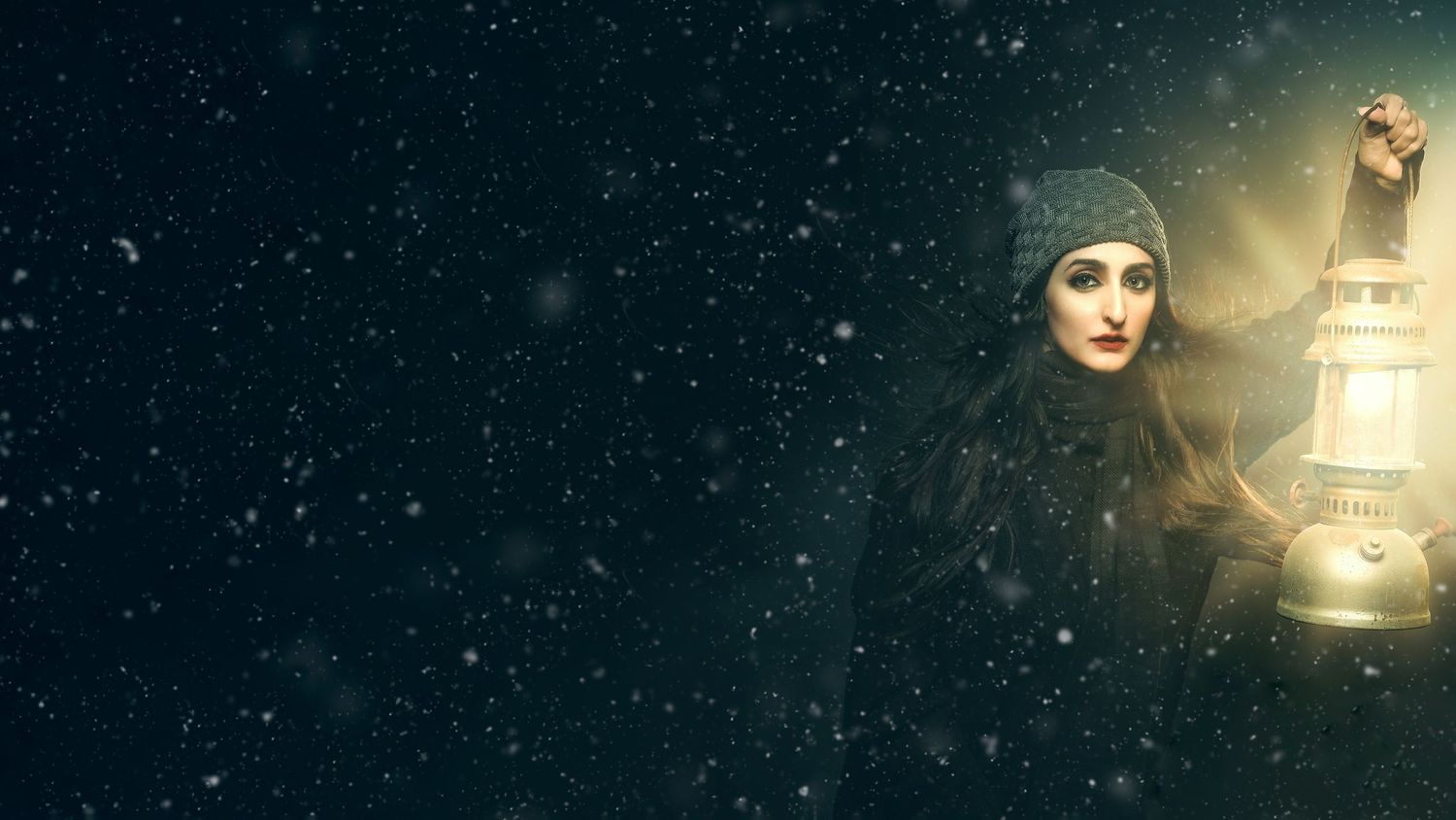 A mysterious woman in dark winter clothing holds a glowing lantern in a snowy night scene.