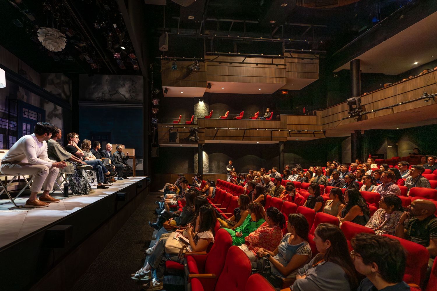 Large audience fills red theater seats during panel discussion on stage at conference.