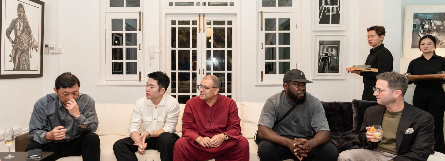 A diverse group of people sit together in conversation in an elegant white room with artwork on the walls.