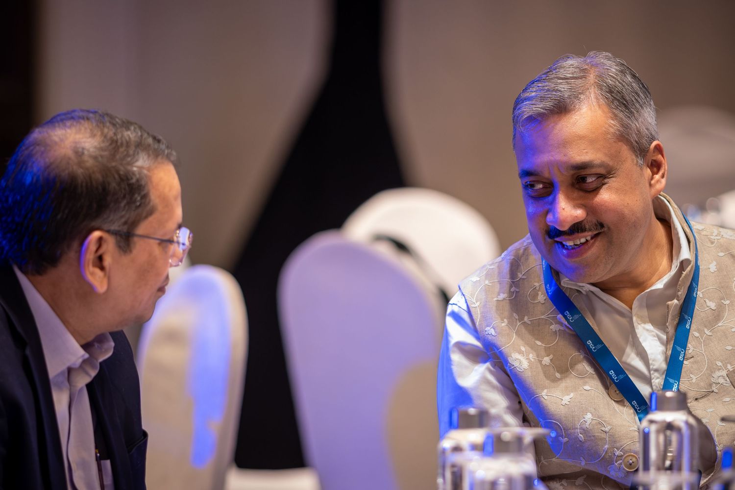 Two men in formal attire smile and converse at a conference dinner event.