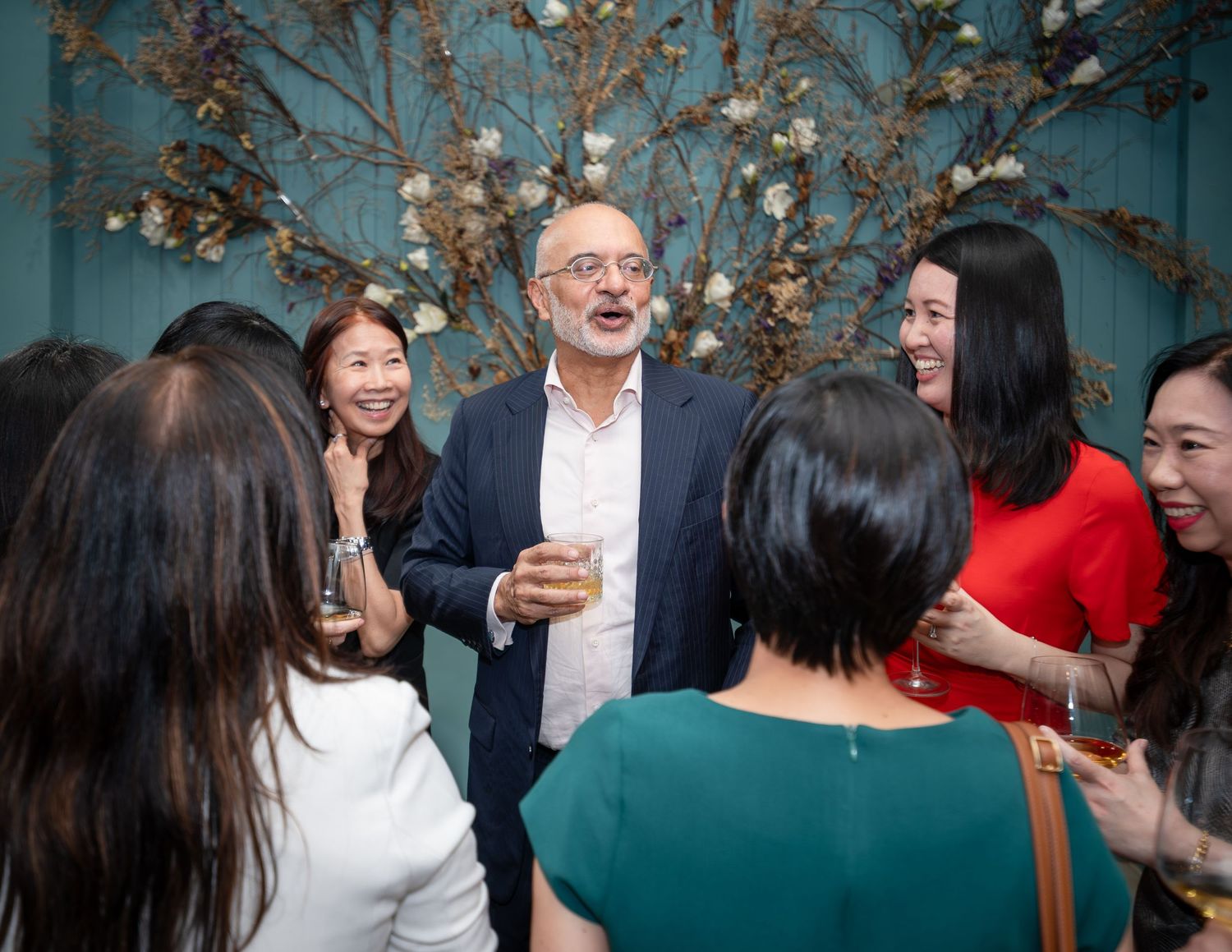 Man in blazer socializing with group of women at elegant indoor party event.