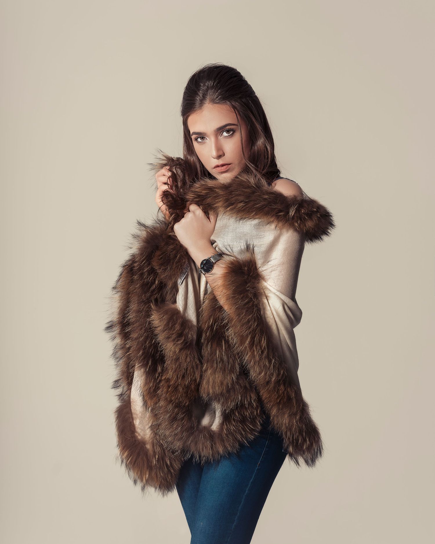 Young woman posing in brown fur vest over silk top with blue jeans and watch, studio fashion shot.