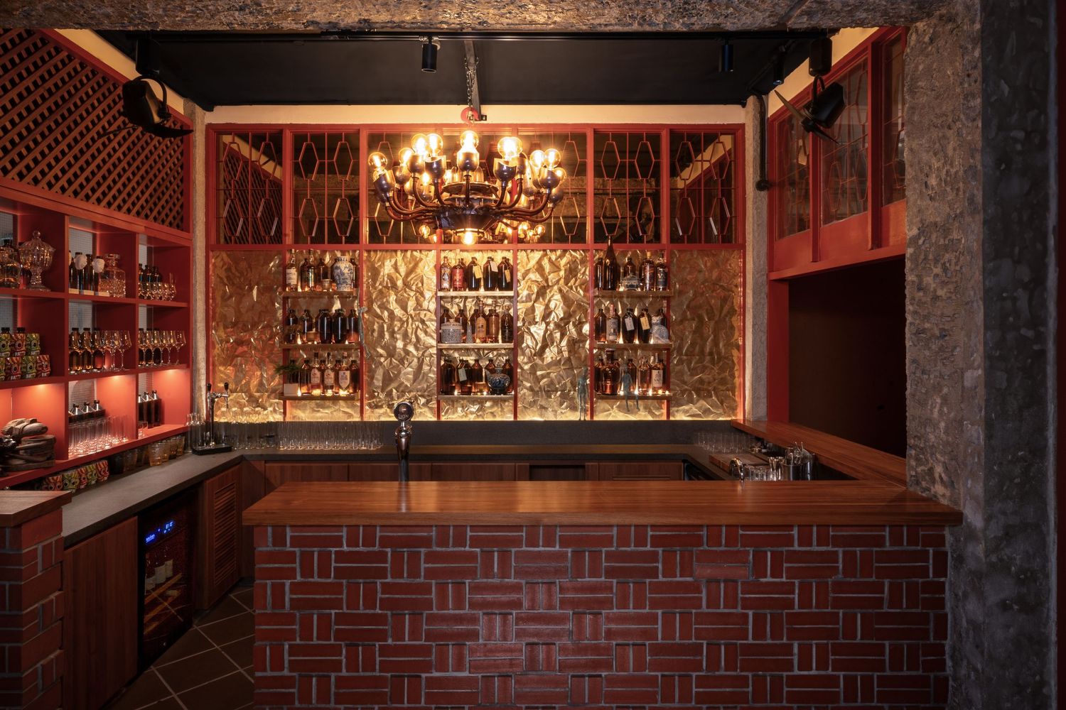 Elegant red brick bar with chandelier and backlit wine bottle display wall.