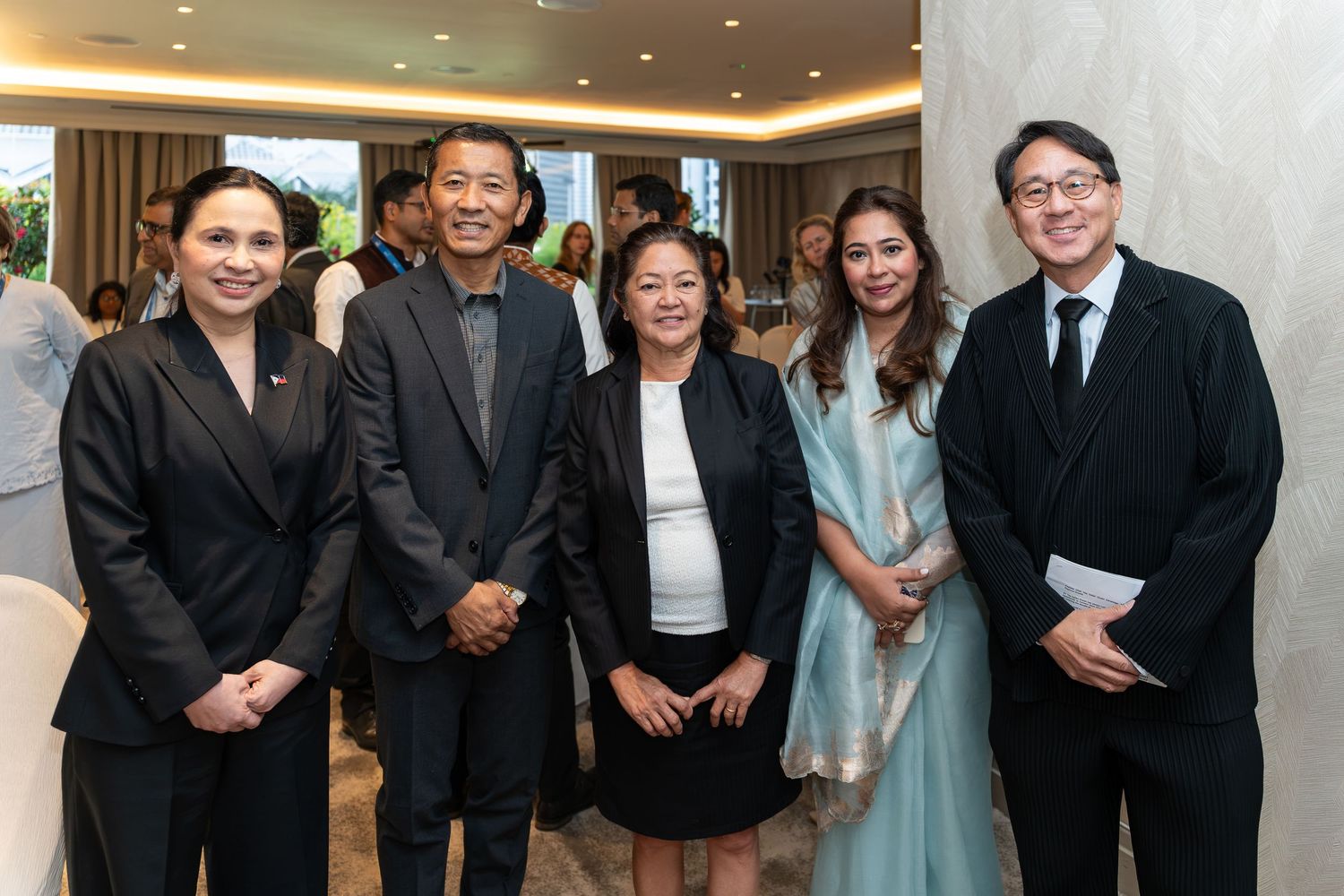 Five formally dressed professionals posing together at an elegant indoor event or ceremony.
