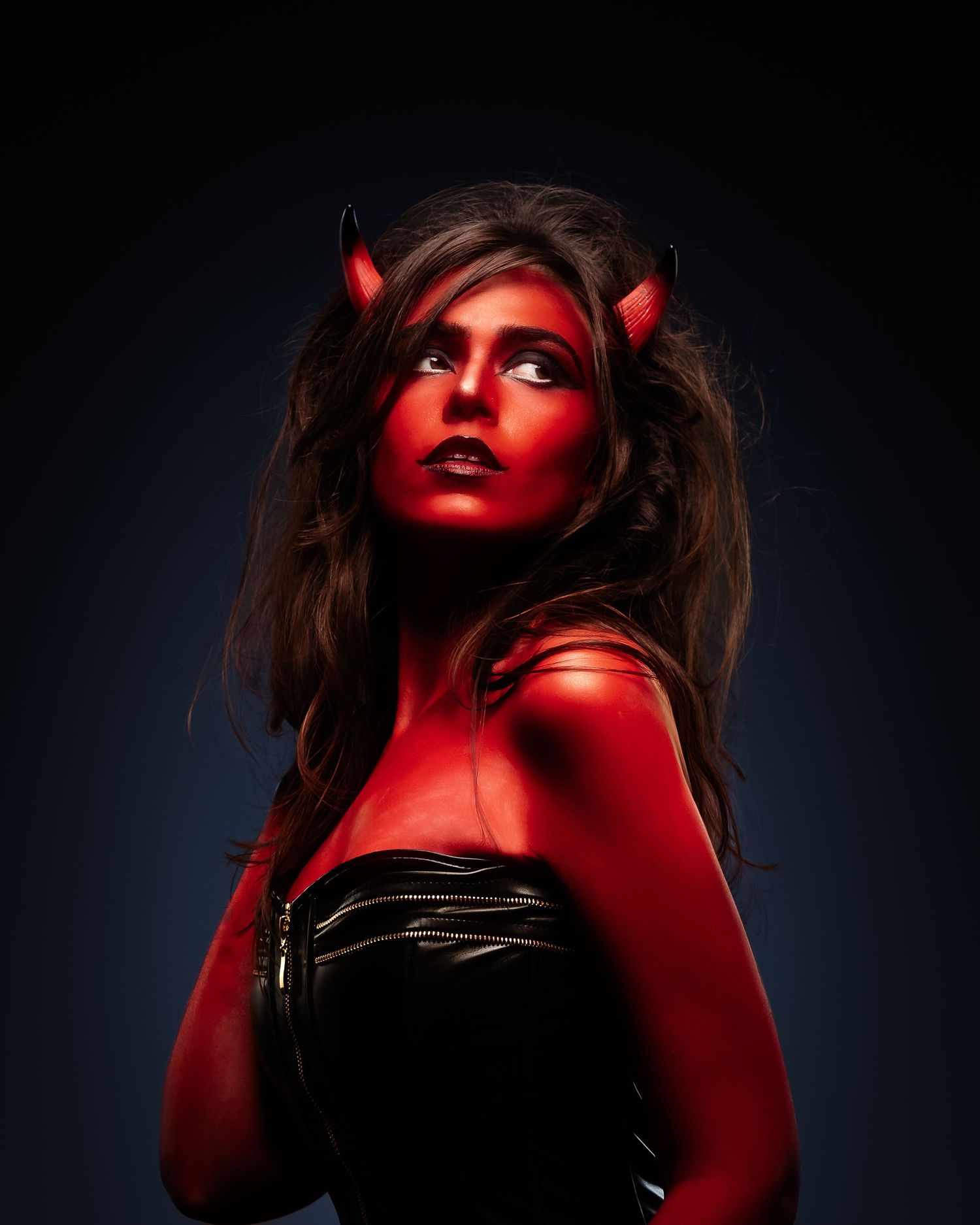 Woman in devil Halloween costume with red body paint, horns, and black strapless top posing dramatically.