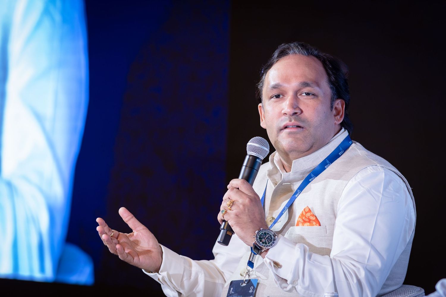 Man in white shirt speaking at conference event holding microphone gesturing with hand.