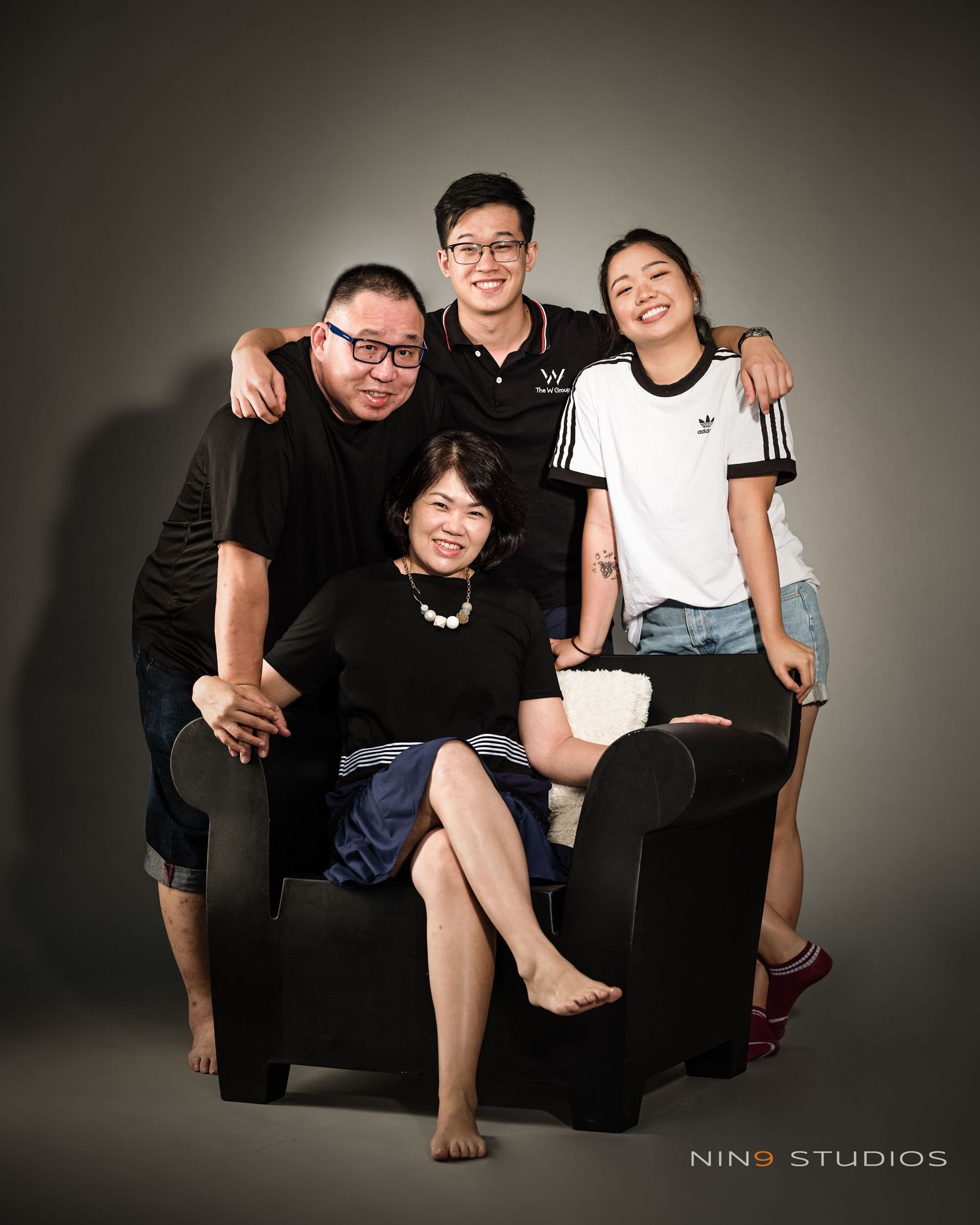 Family of four posing for a studio portrait at Nino Studios, smiling warmly together around a black armchair.
