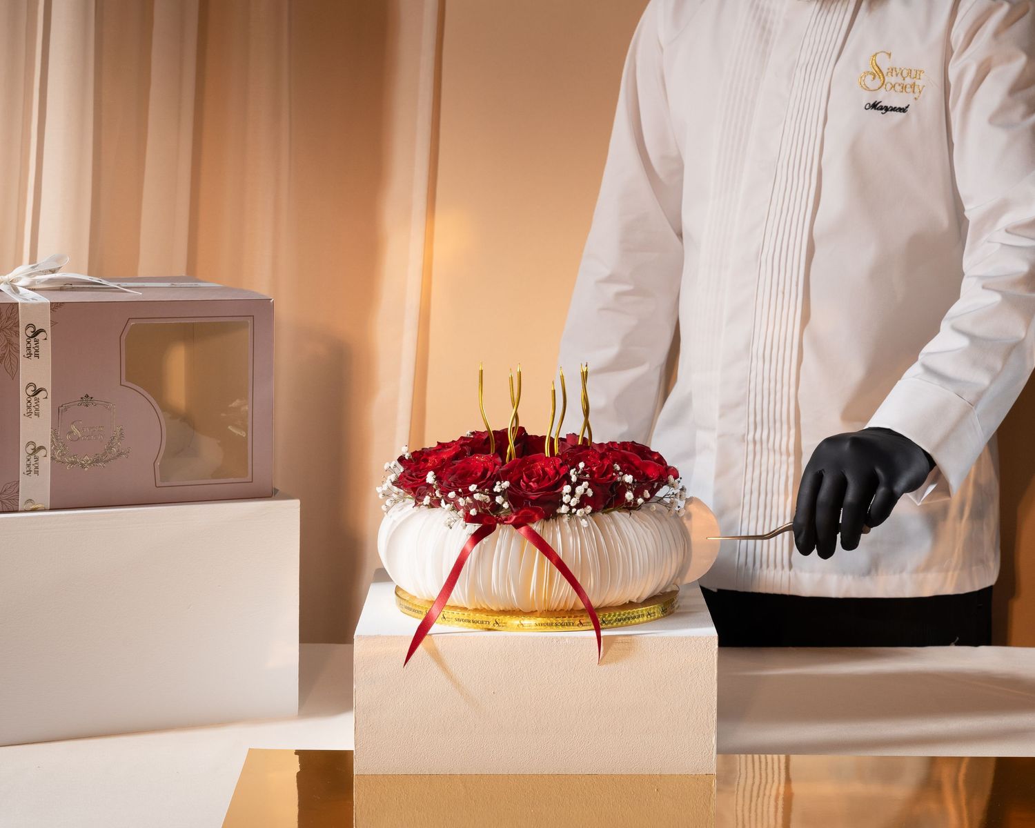 Hotel staff presenting an elegant cake adorned with red roses and gold candles on a white pedestal.