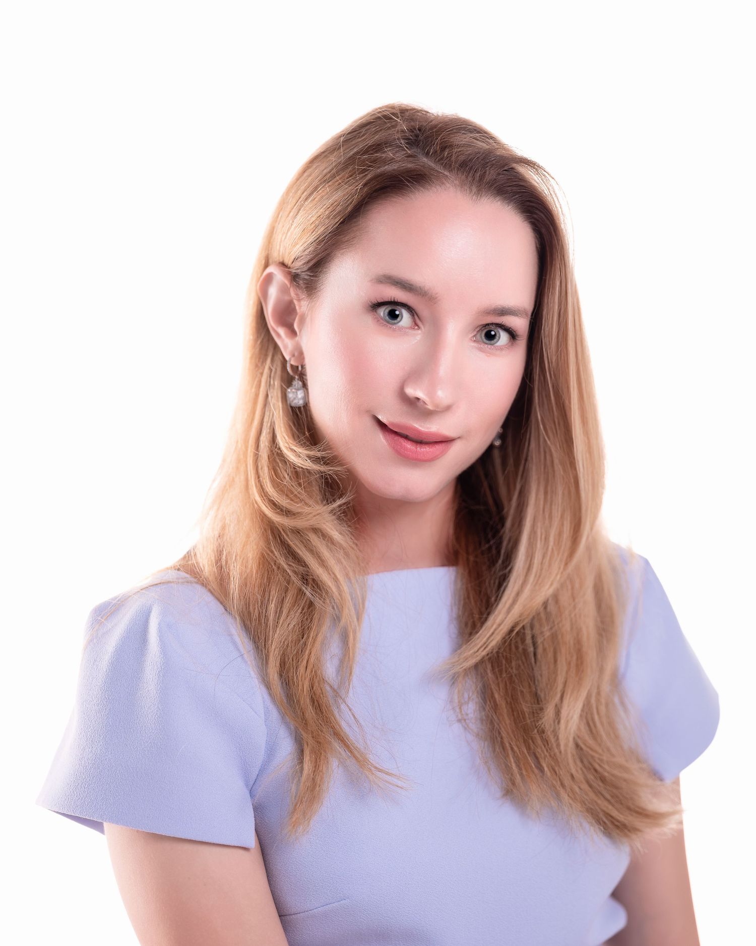 Professional headshot of a smiling young woman with blonde hair wearing a light blue top and pearl drop earrings.