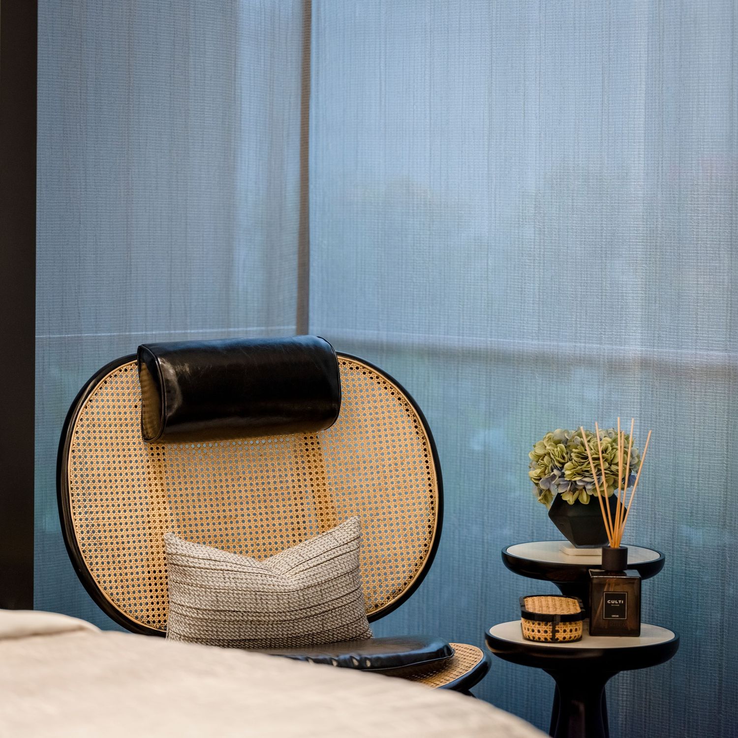 Rattan circular chair with black leather headrest beside a small round table with reed diffuser.