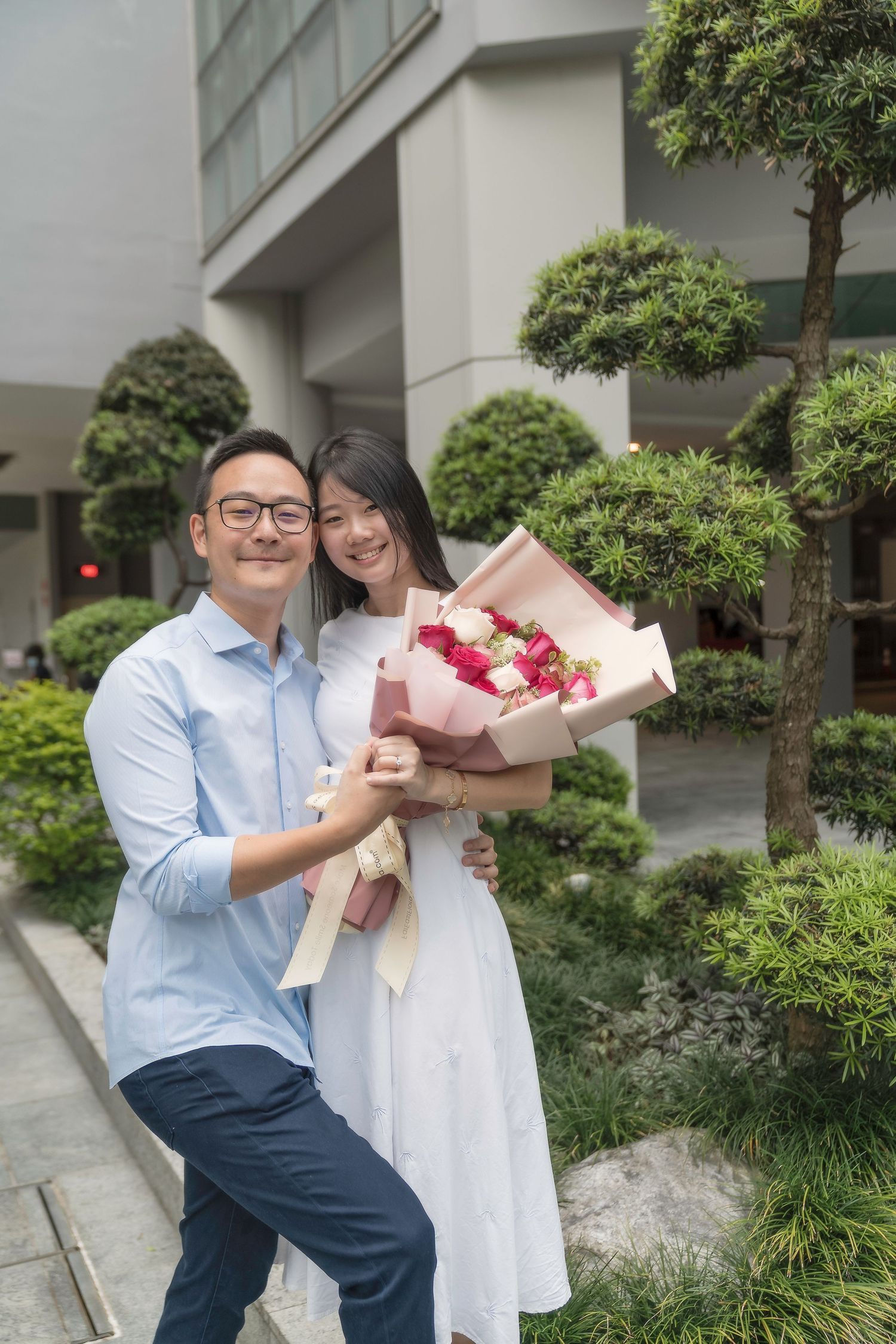 Happy Asian couple embracing outdoors while holding a bouquet of red and white roses.