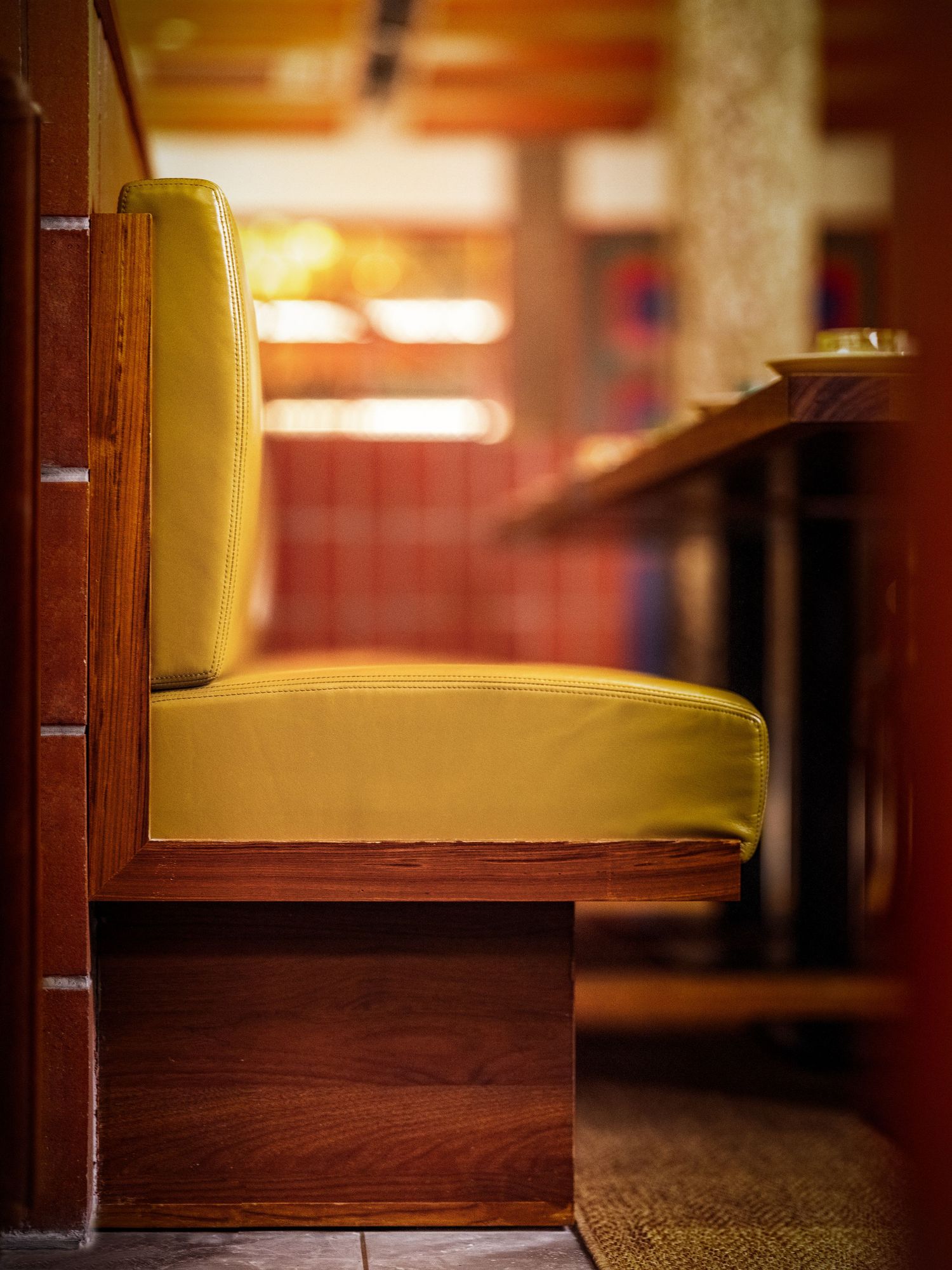 Yellow upholstered booth seat with wooden frame in a warm-toned restaurant interior.