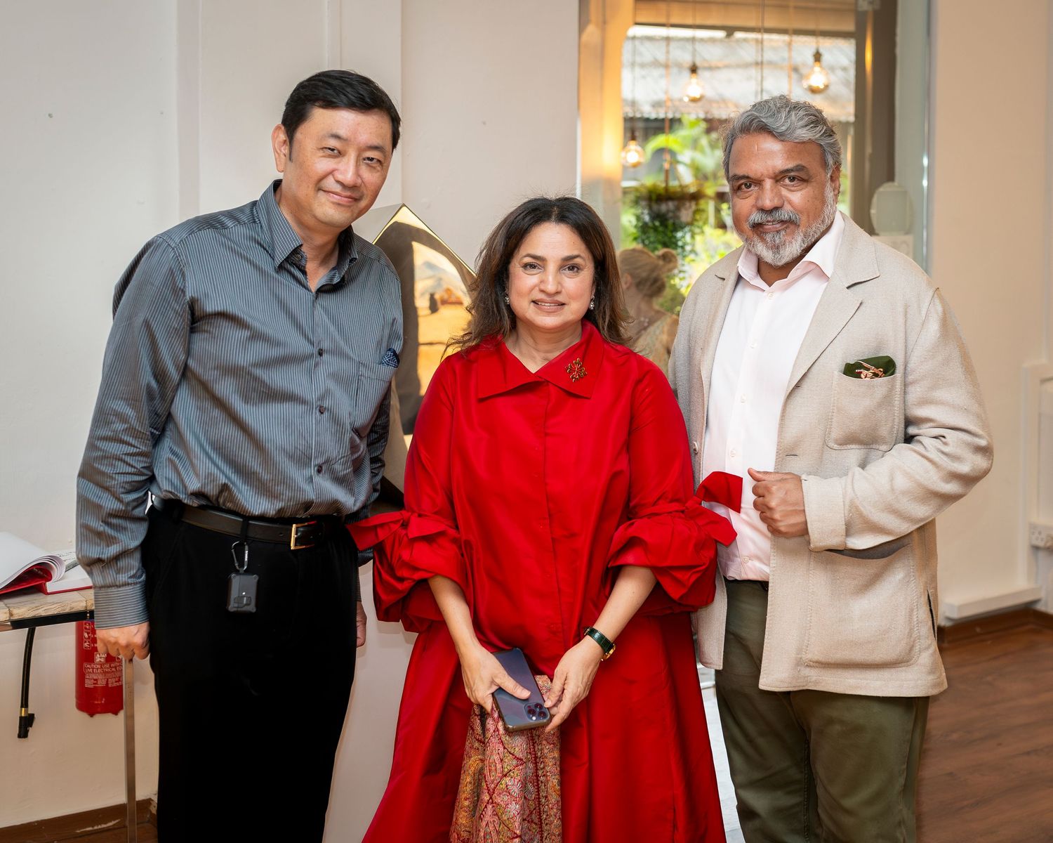 Three guests posing together at art gallery opening event indoors.